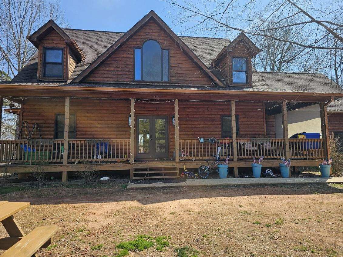 Wooden cabin with porch, two dormers. Front door, windows. Blue pots line the porch.