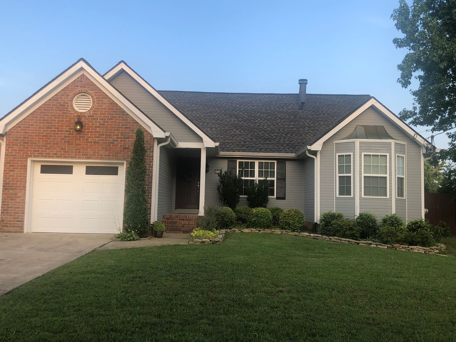 A gray house with a brick accent, white garage door, and green lawn under a blue sky.