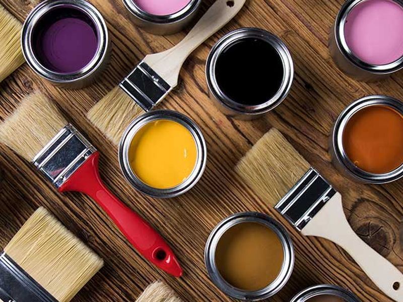 Paint cans of various colors with paint brushes arranged on a wooden surface.