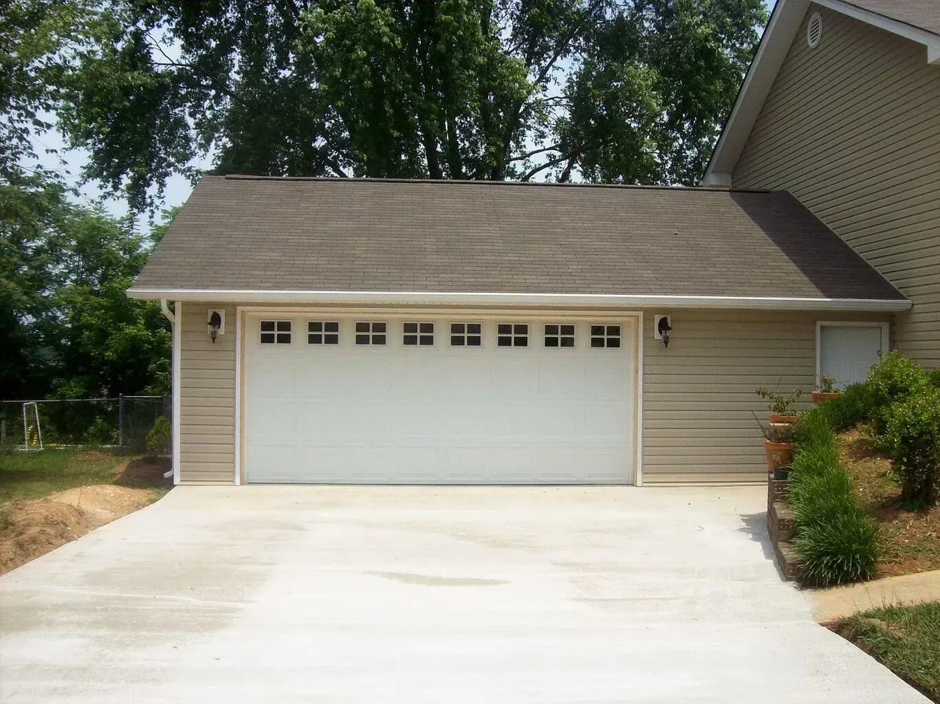 Tan garage with white door, concrete driveway, and beige siding next to a house.