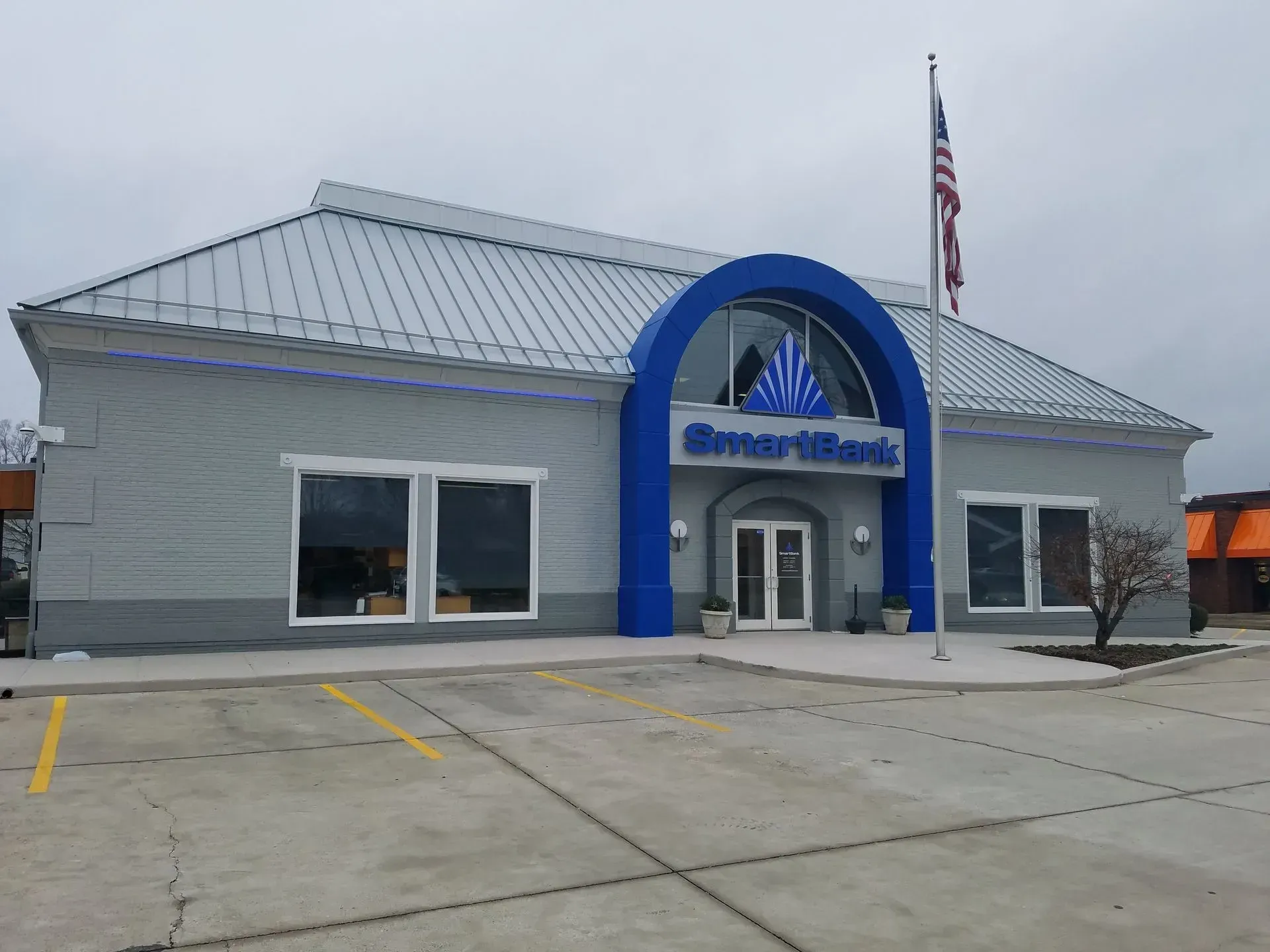 Bank building with a blue arch over the entrance, a silver roof, and an American flag in front.