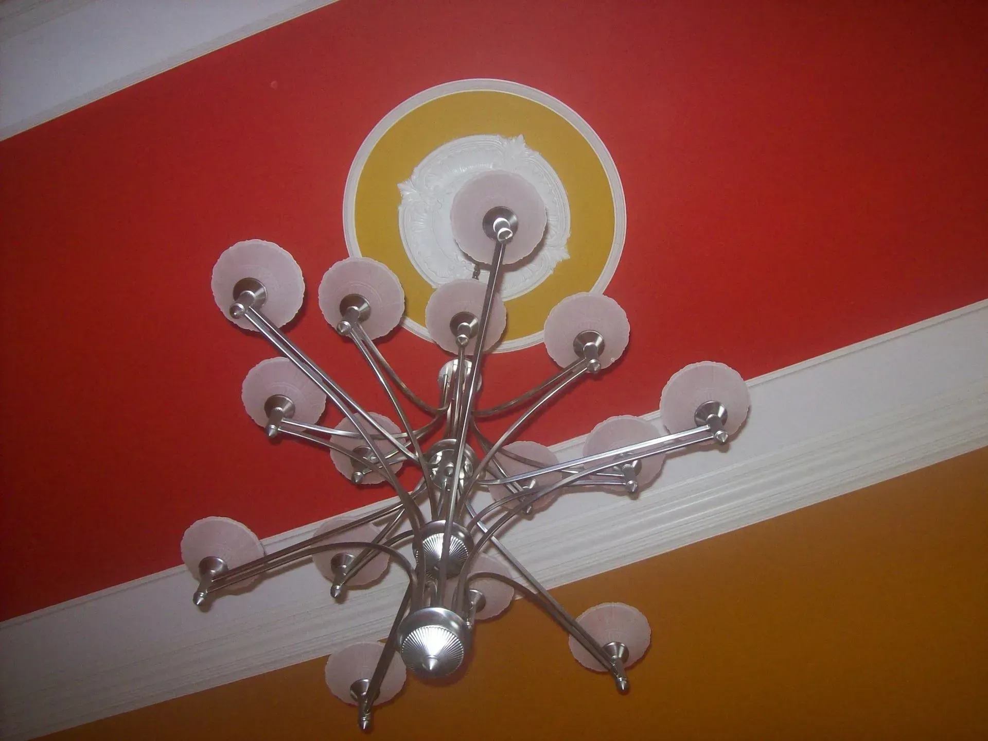Silver chandelier hangs from a red and yellow ceiling with a circular, decorative detail.