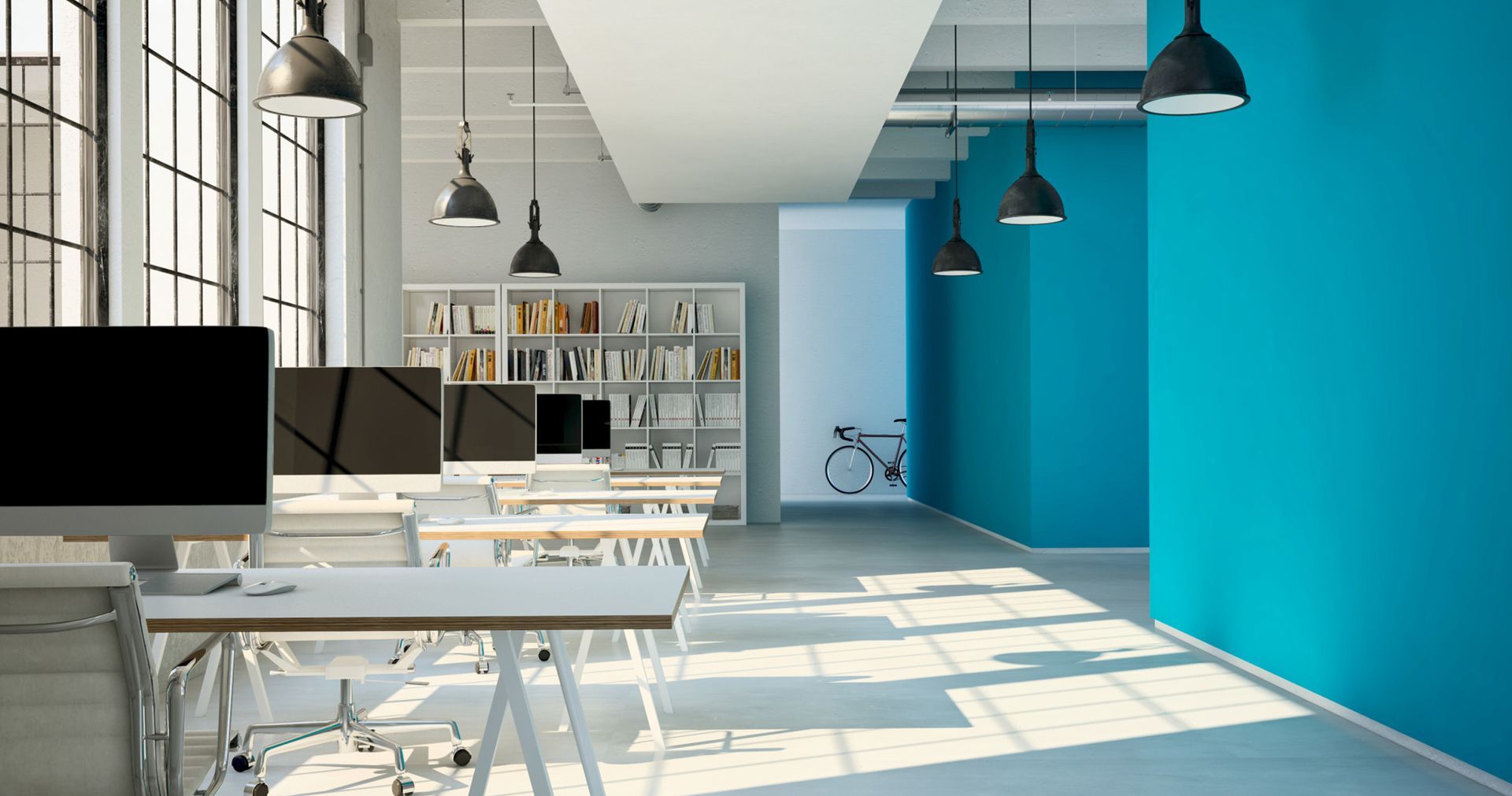 Modern office space with white desks, teal wall, and black hanging lights.