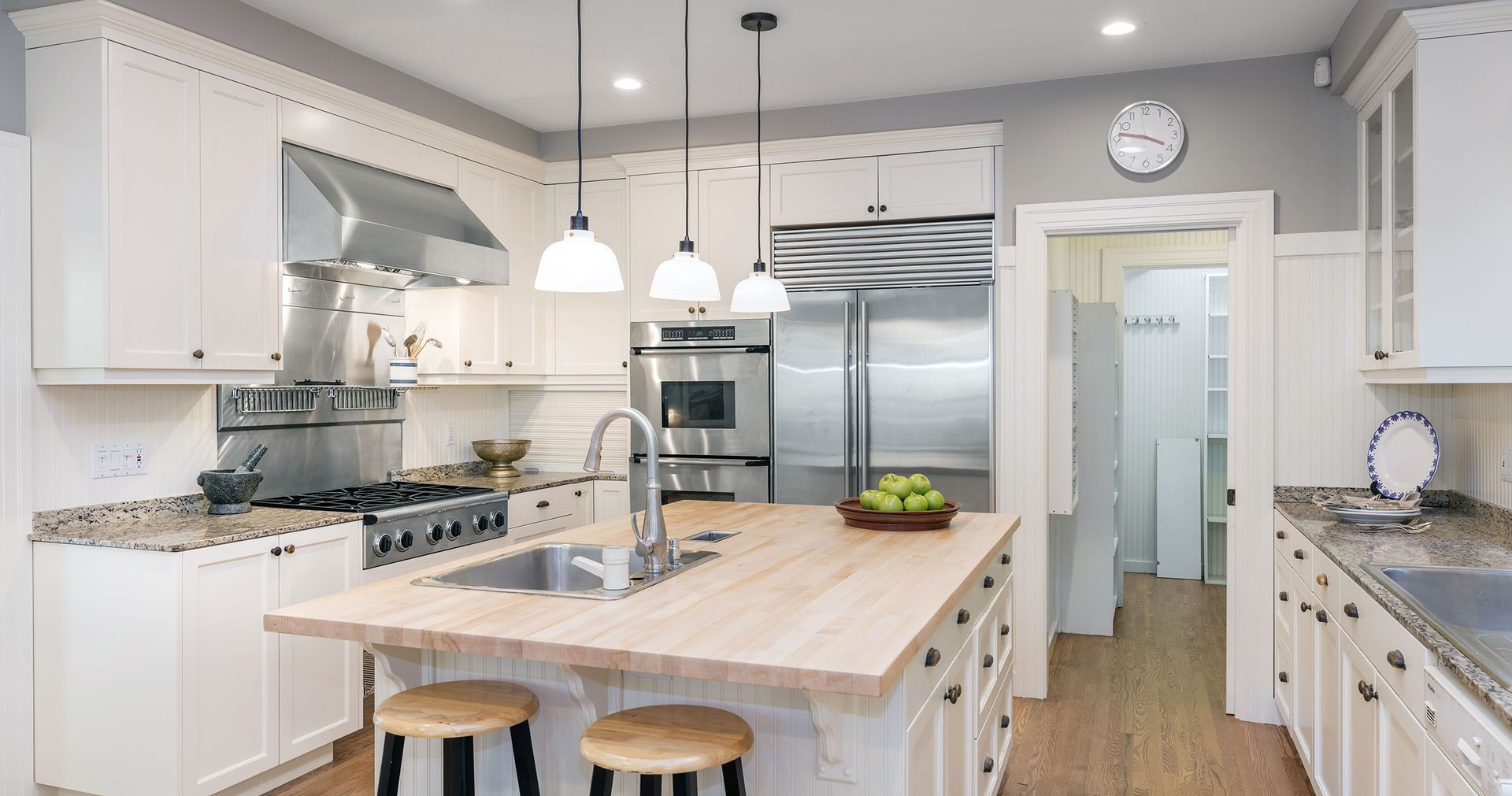 White kitchen with island, stainless steel appliances, light wood countertops, and grey walls.