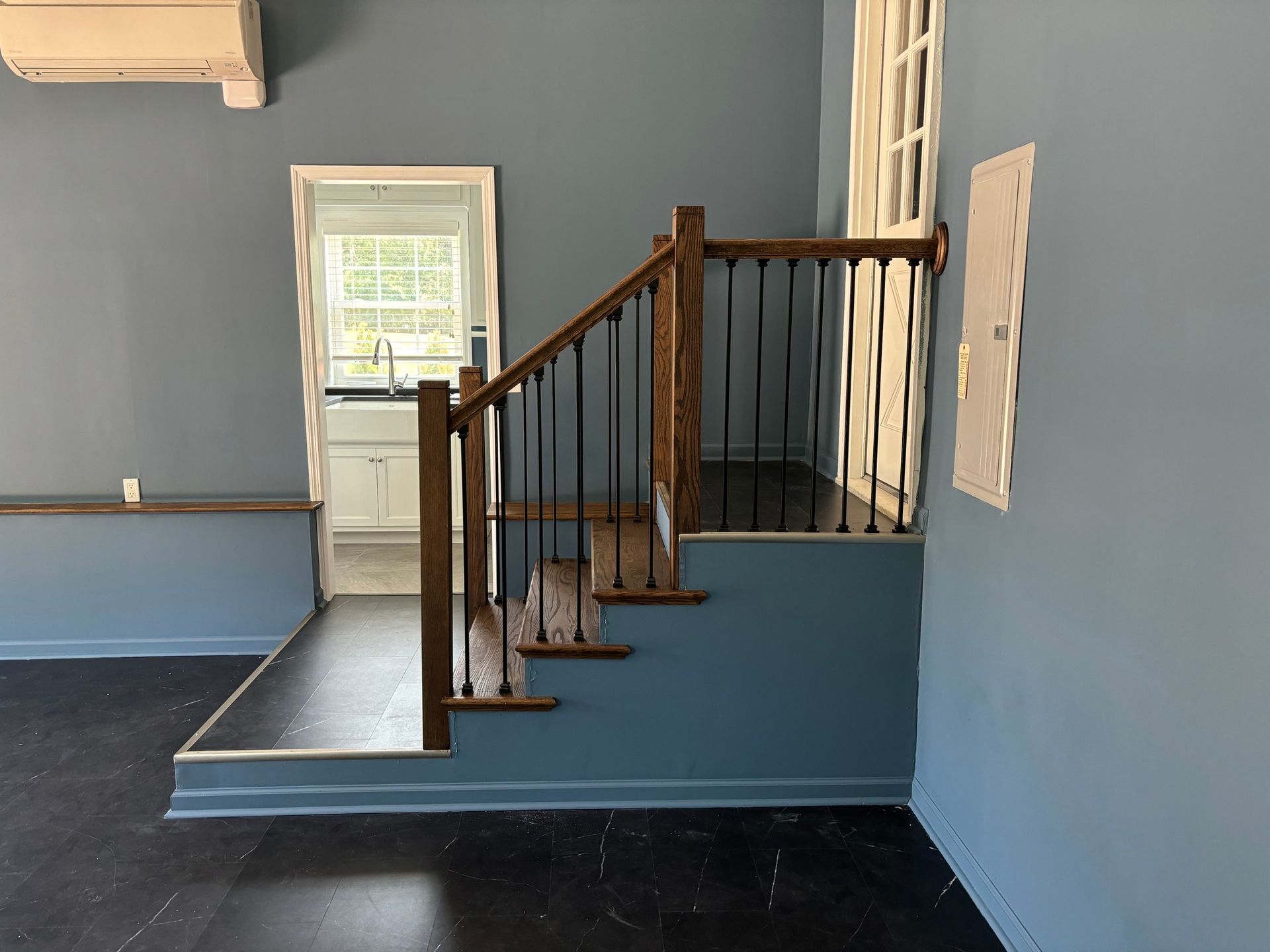 Staircase with dark wood handrail and black spindles, blue walls, leading to a kitchen with a window.