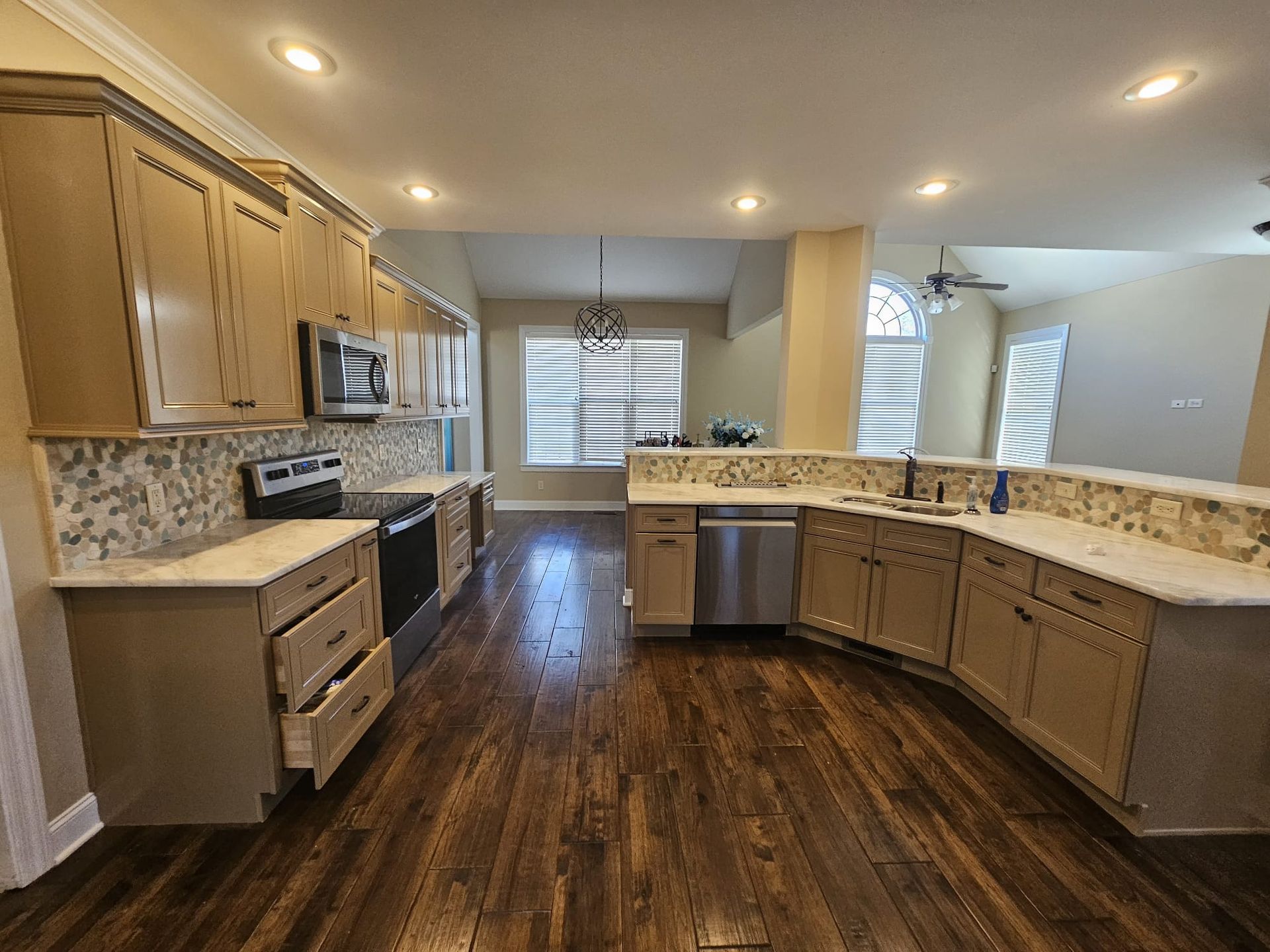 Spacious kitchen with light wood cabinets, stainless steel appliances, and dark wood floors.