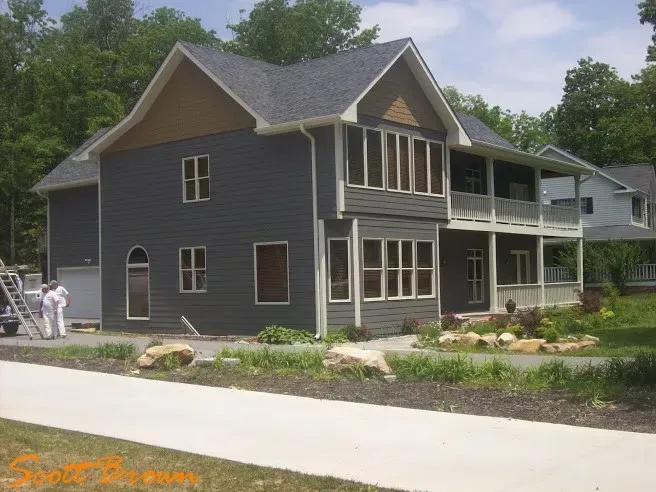Two-story house with gray siding and brown trim, featuring balconies and a stone pathway in front.
