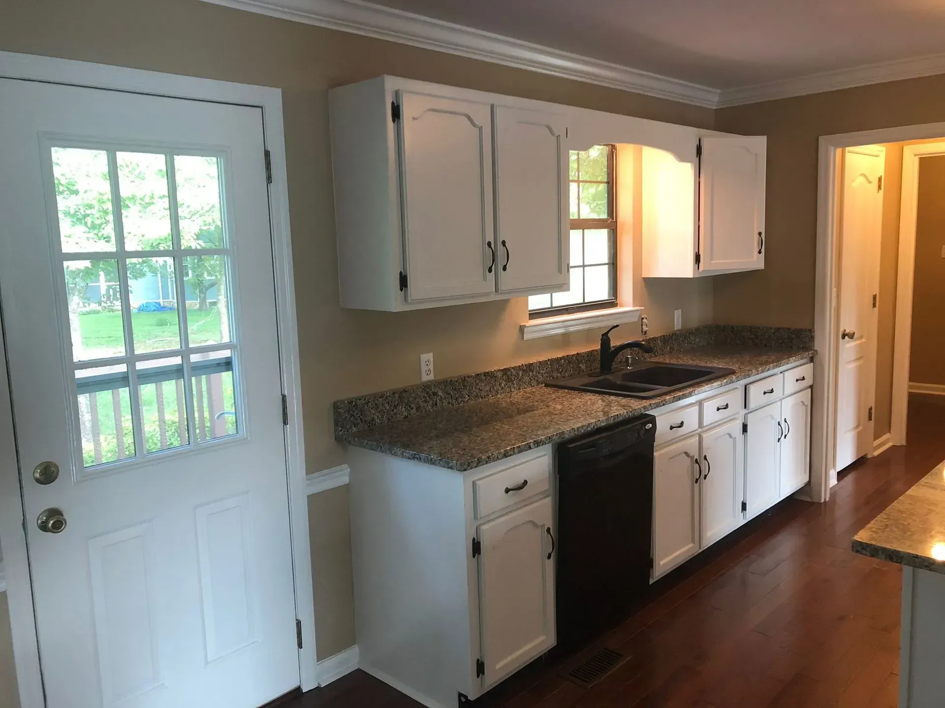 White kitchen cabinets with granite countertops, dishwasher, and glass door.