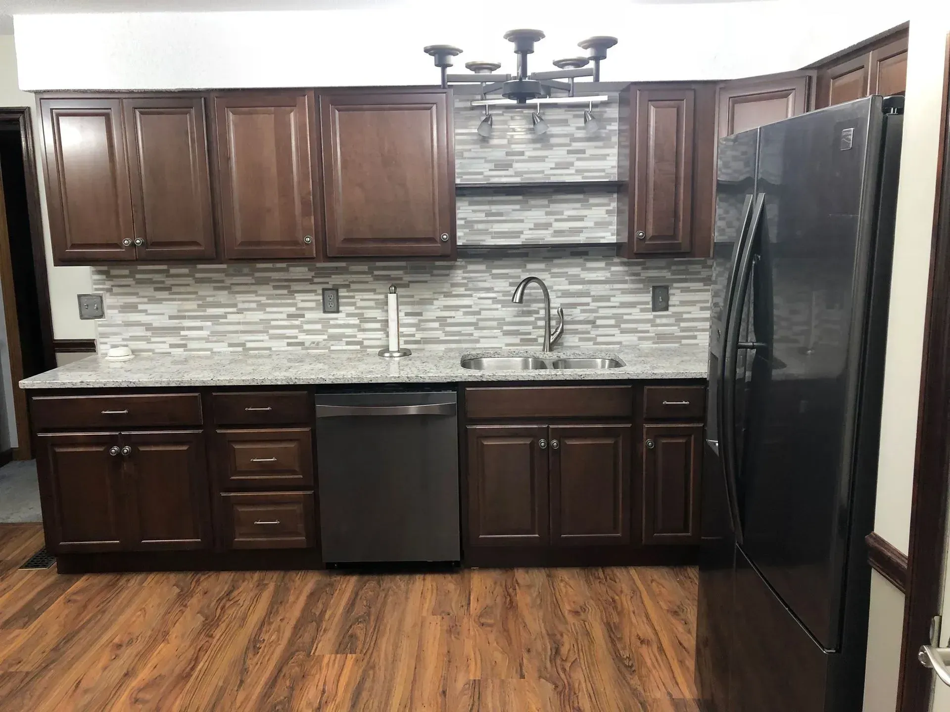 Kitchen with dark brown cabinets, granite countertop, silver appliances, and a mosaic backsplash.
