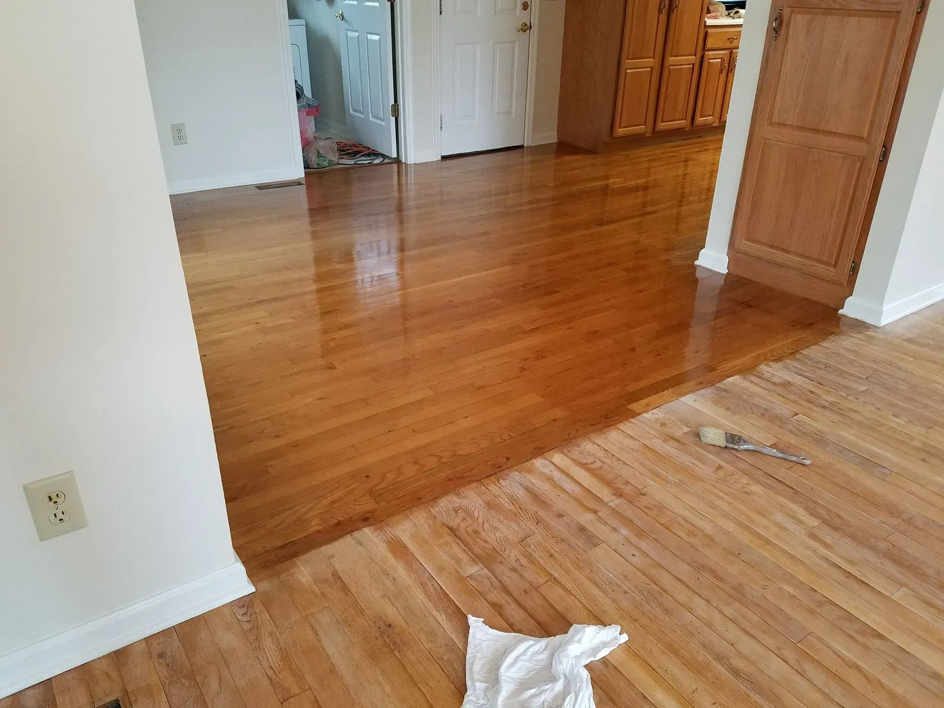 Hardwood floors, partially finished with glossy stain. A brush and cloth lay on the floor.