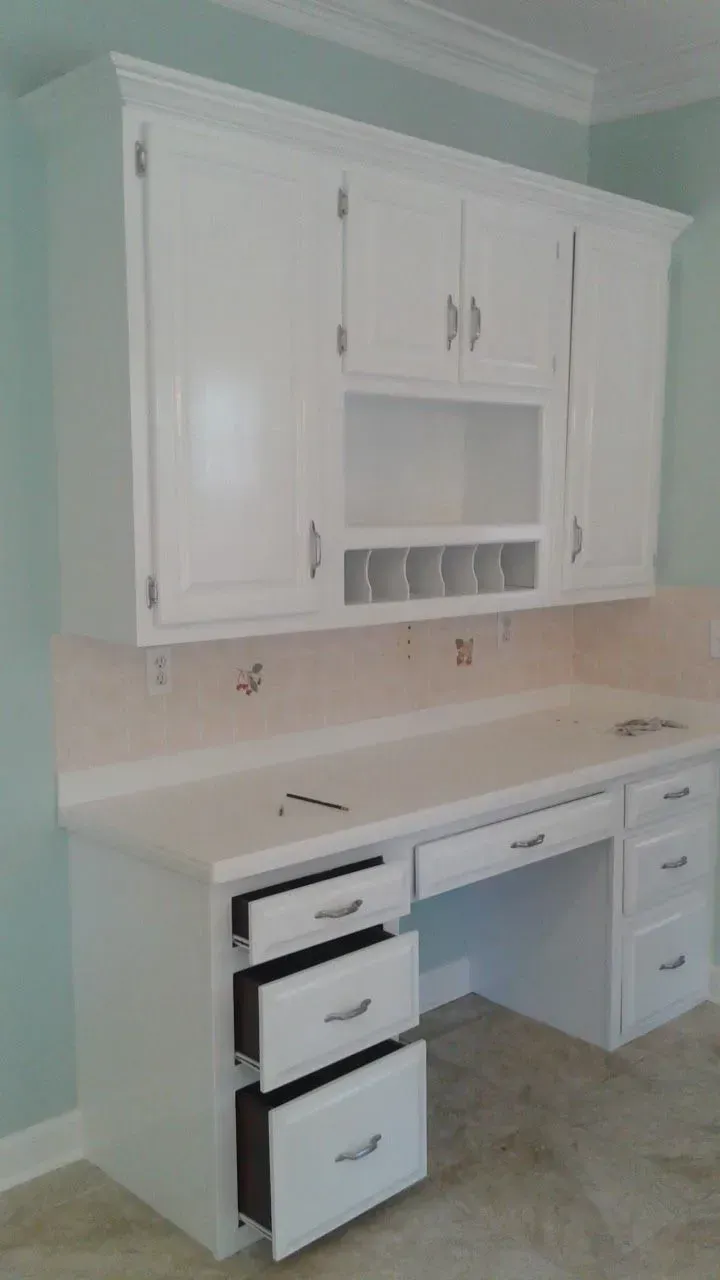 White built-in desk and cabinets with open drawers. Desk has upper cabinets with a shelf.
