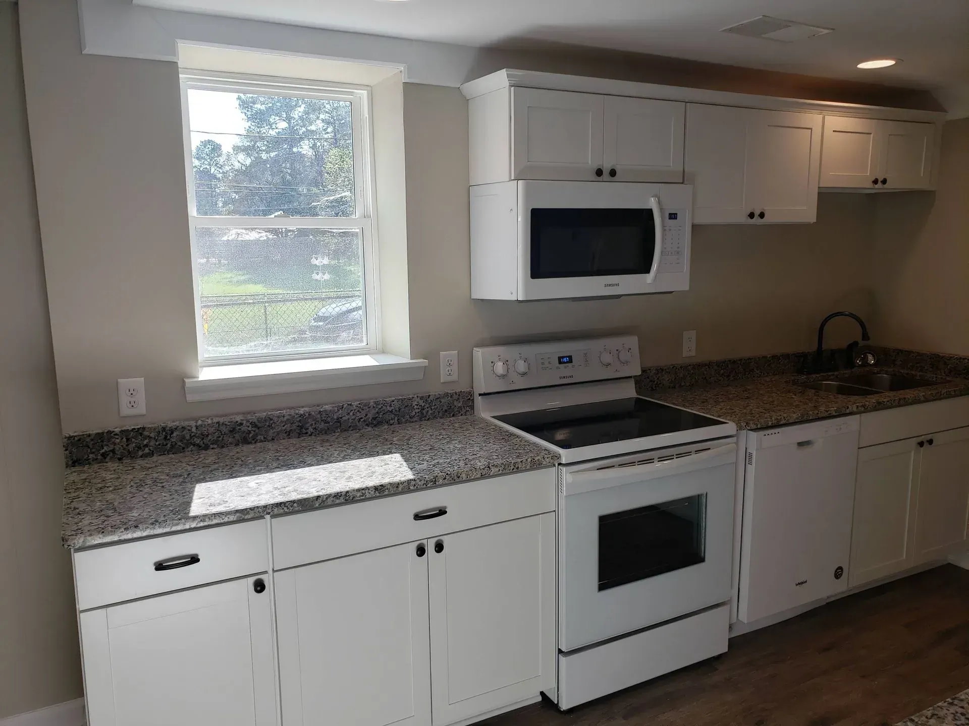 Small kitchen with white cabinets, granite countertops, and a window.