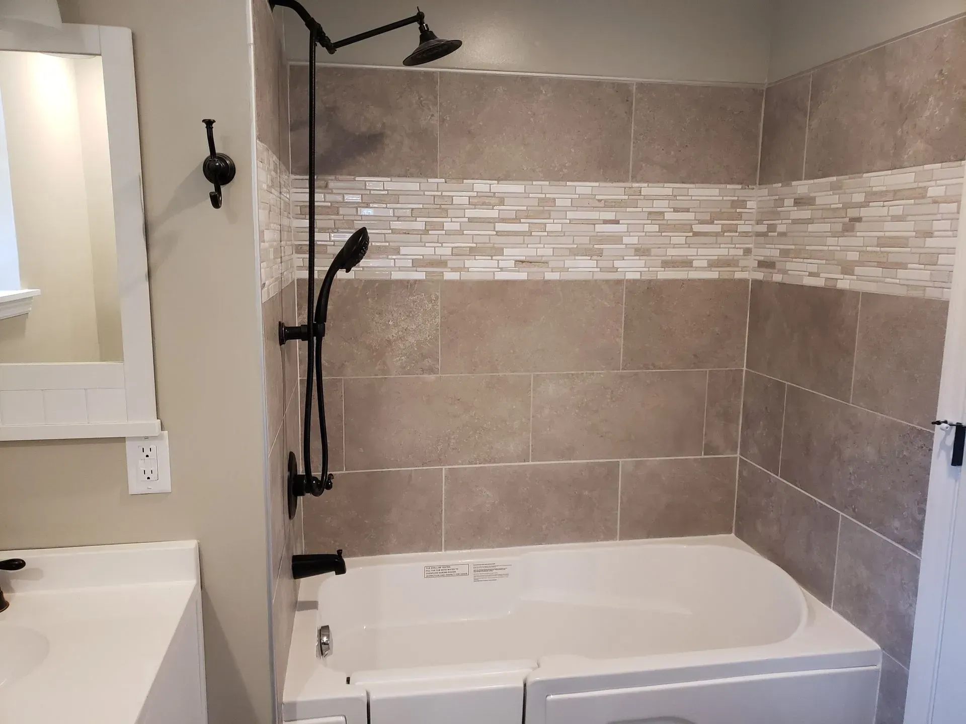 Bathroom with a bathtub and showerhead, beige tiles, and dark fixtures.