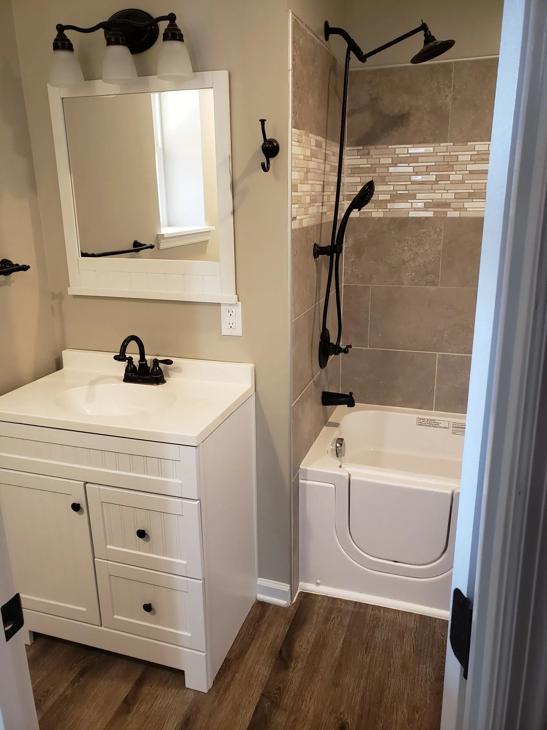 Accessible bathroom with white vanity, step-in tub, dark fixtures, and neutral tile.
