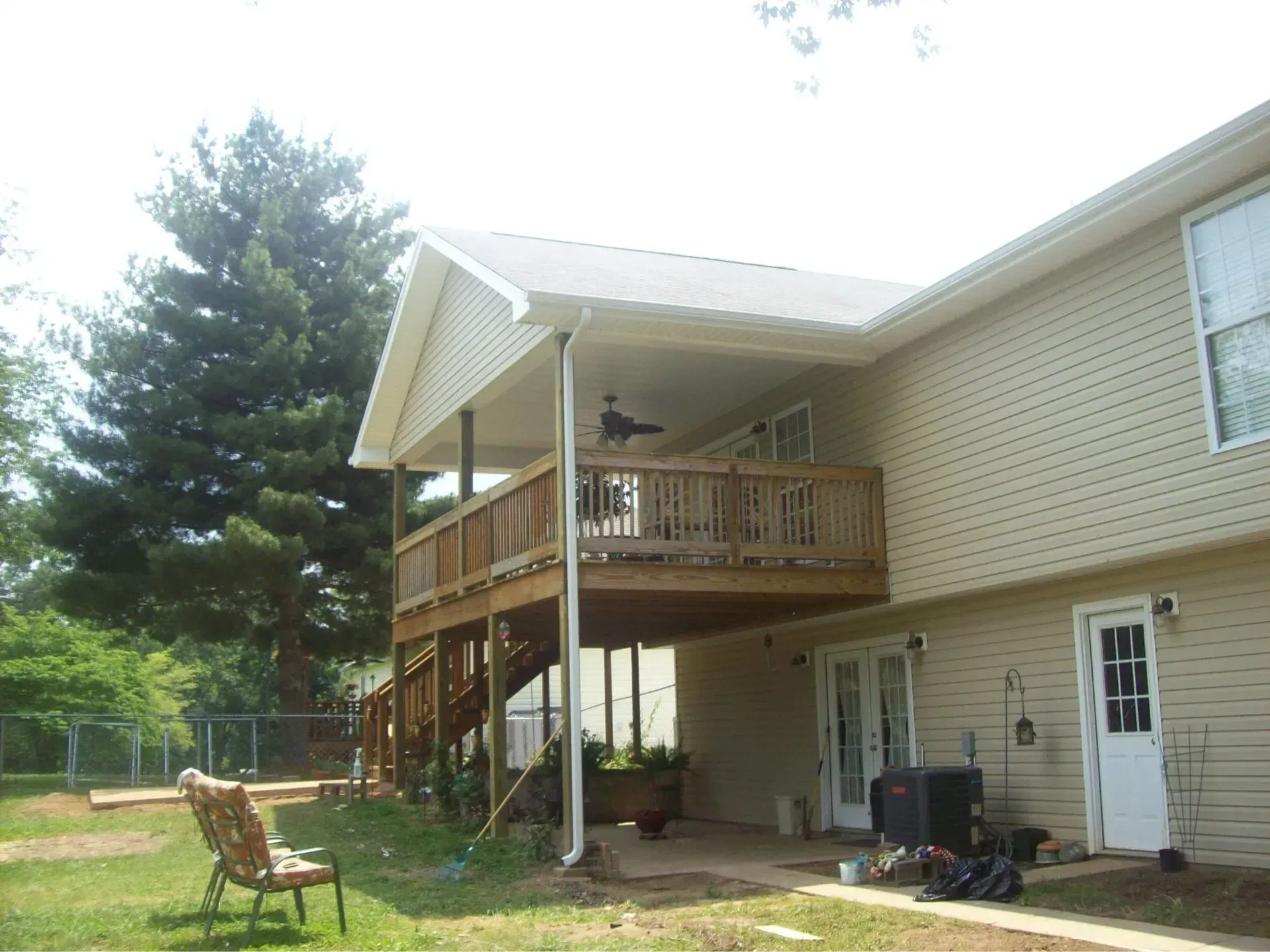 Two-story house with a deck. Tan siding, white roof.  A wooden deck extends from the second story. Green grass with a chair.