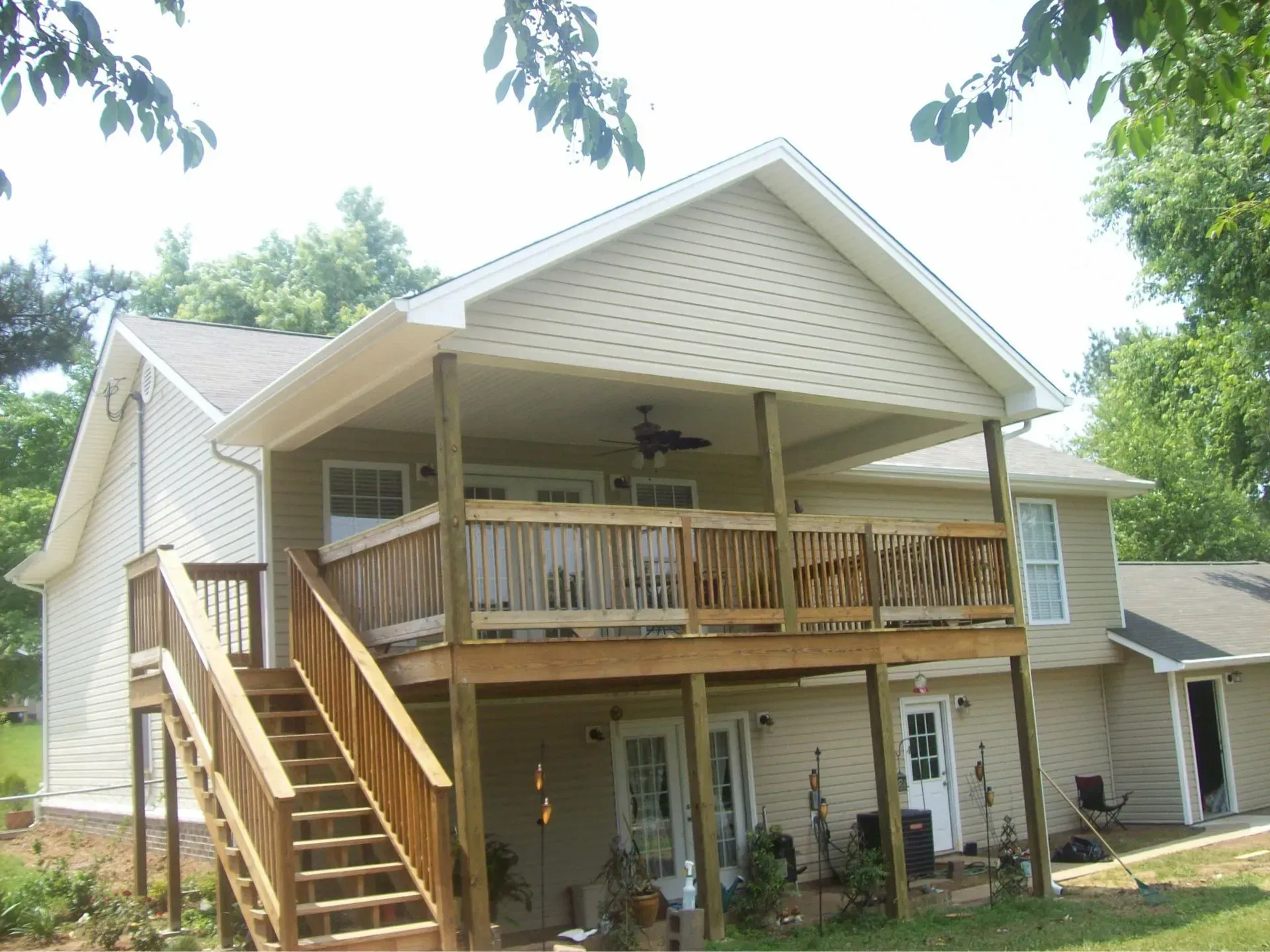 Two-story house with wooden deck, stairs, and beige siding, in a yard with trees.