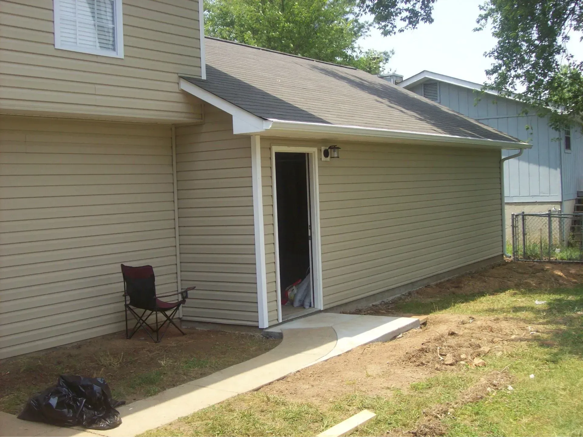Tan siding with a doorway, concrete walkway, and a chair.
