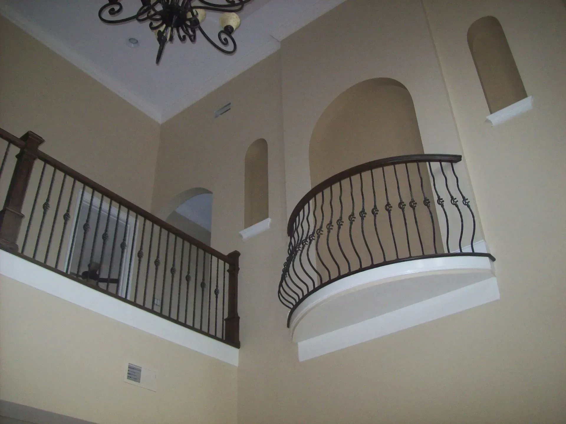Interior view: tan walls, balcony with black railing, arched opening.