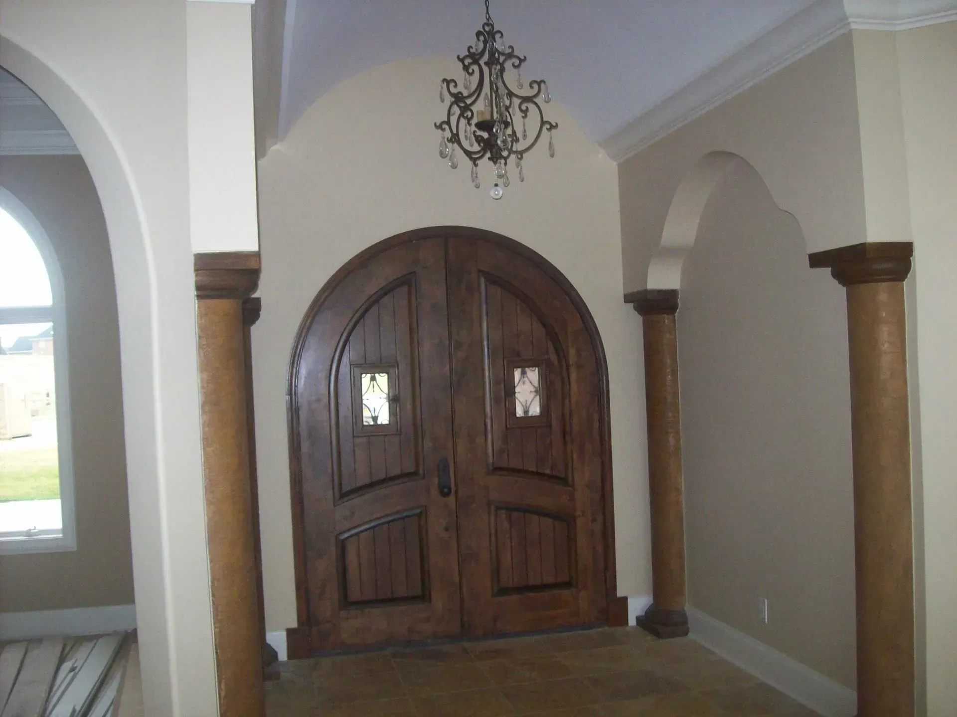 Wooden arched double doors with a chandelier, framed by columns, inside a home.