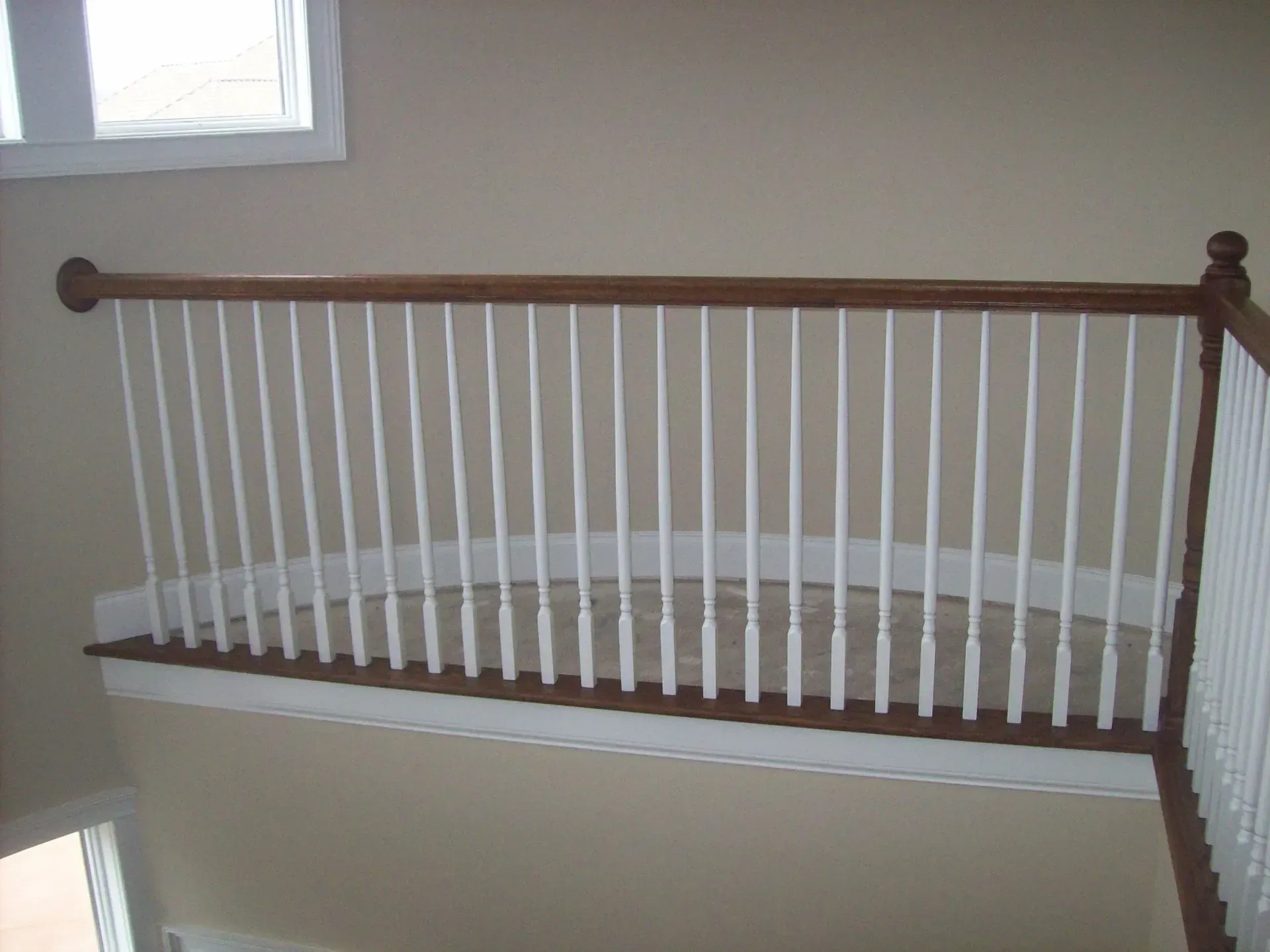 White balustrade with brown handrail on a landing with beige walls and carpet.