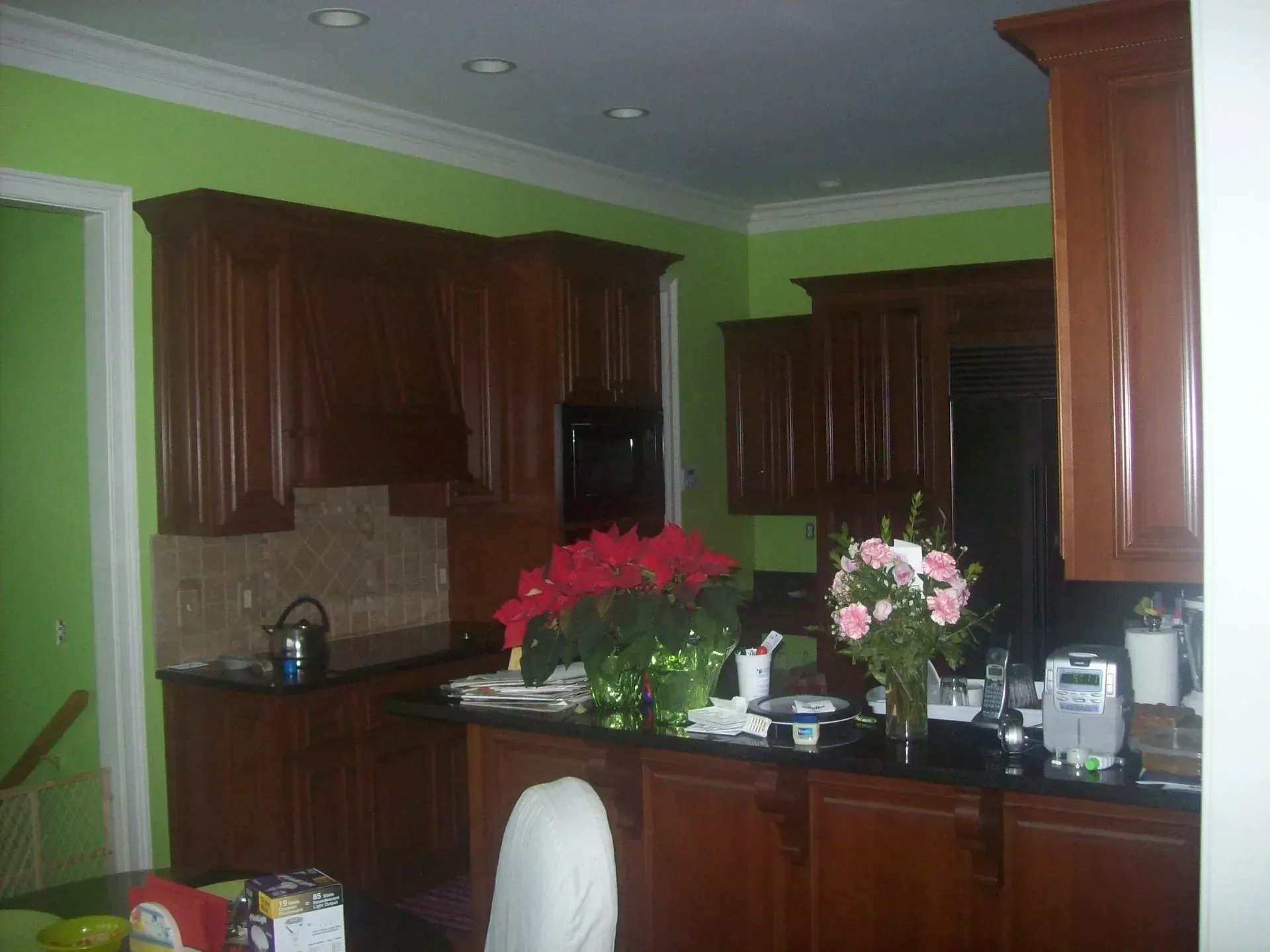 Kitchen with brown cabinets, green walls, and black countertops. Poinsettias and roses on the countertop.