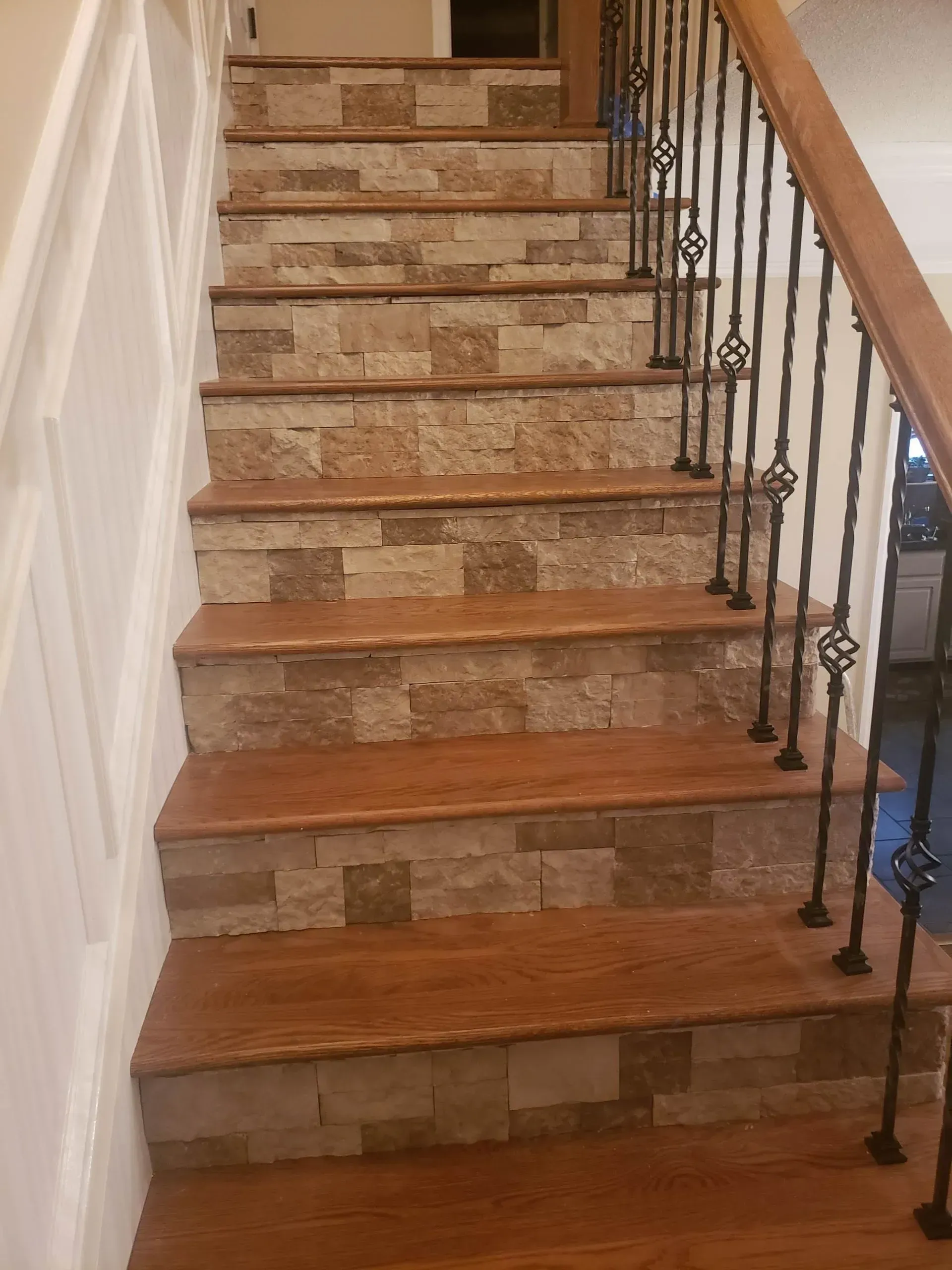 Wooden staircase with stone risers, black iron railing, and tan and brown colors.