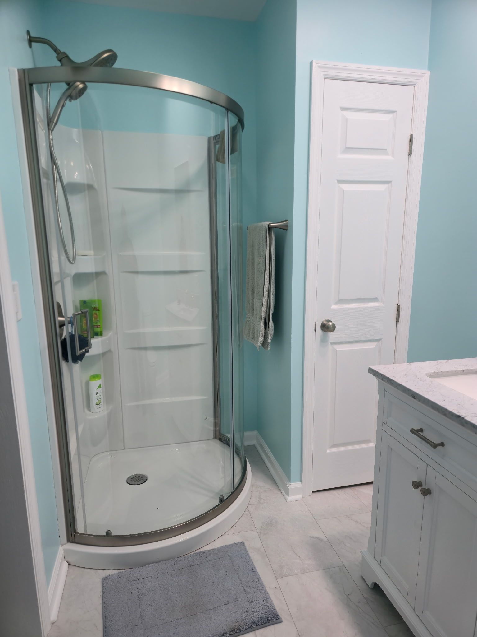 Bathroom with curved glass shower, white door, teal walls, and white vanity.