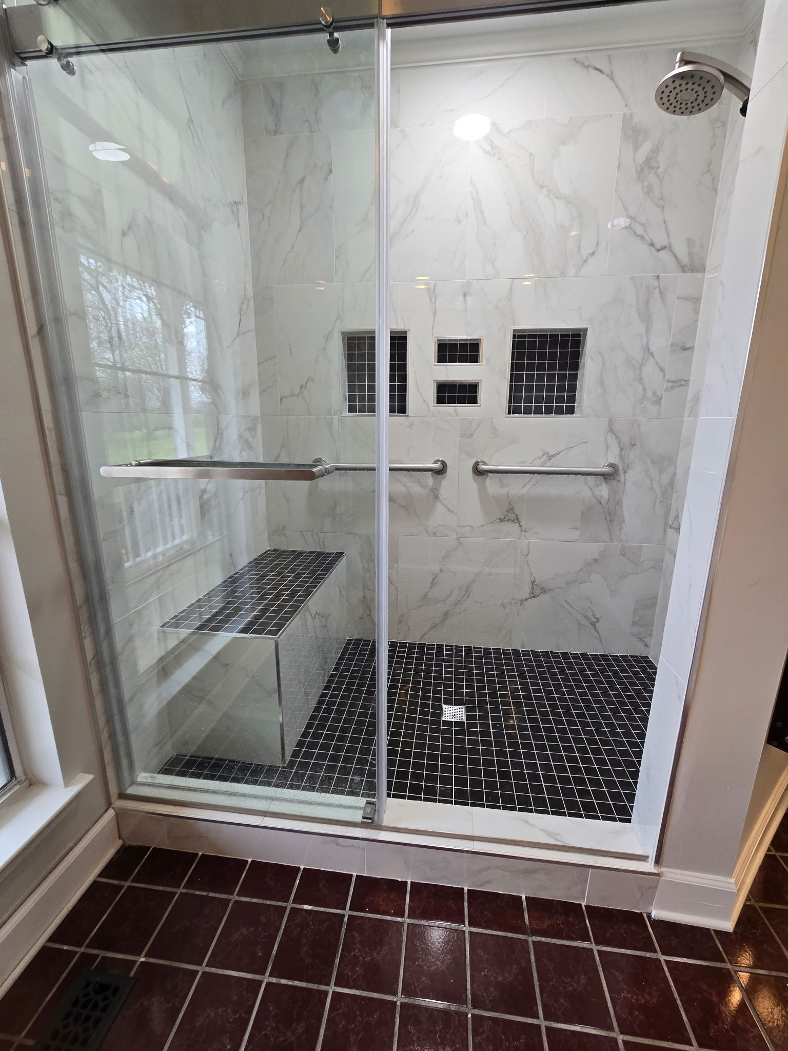 Glass shower enclosure with marble walls, black tile floor, and built-in shelves