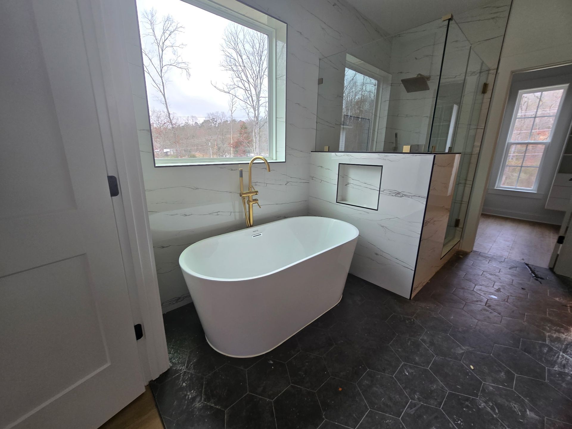 Modern bathroom with freestanding tub, brass faucet, and large window.