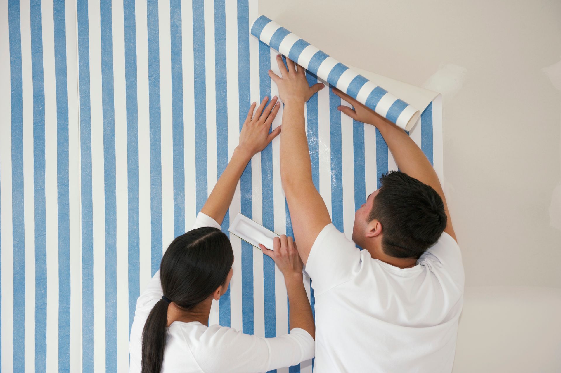 Couple hanging blue and white striped wallpaper on a wall.