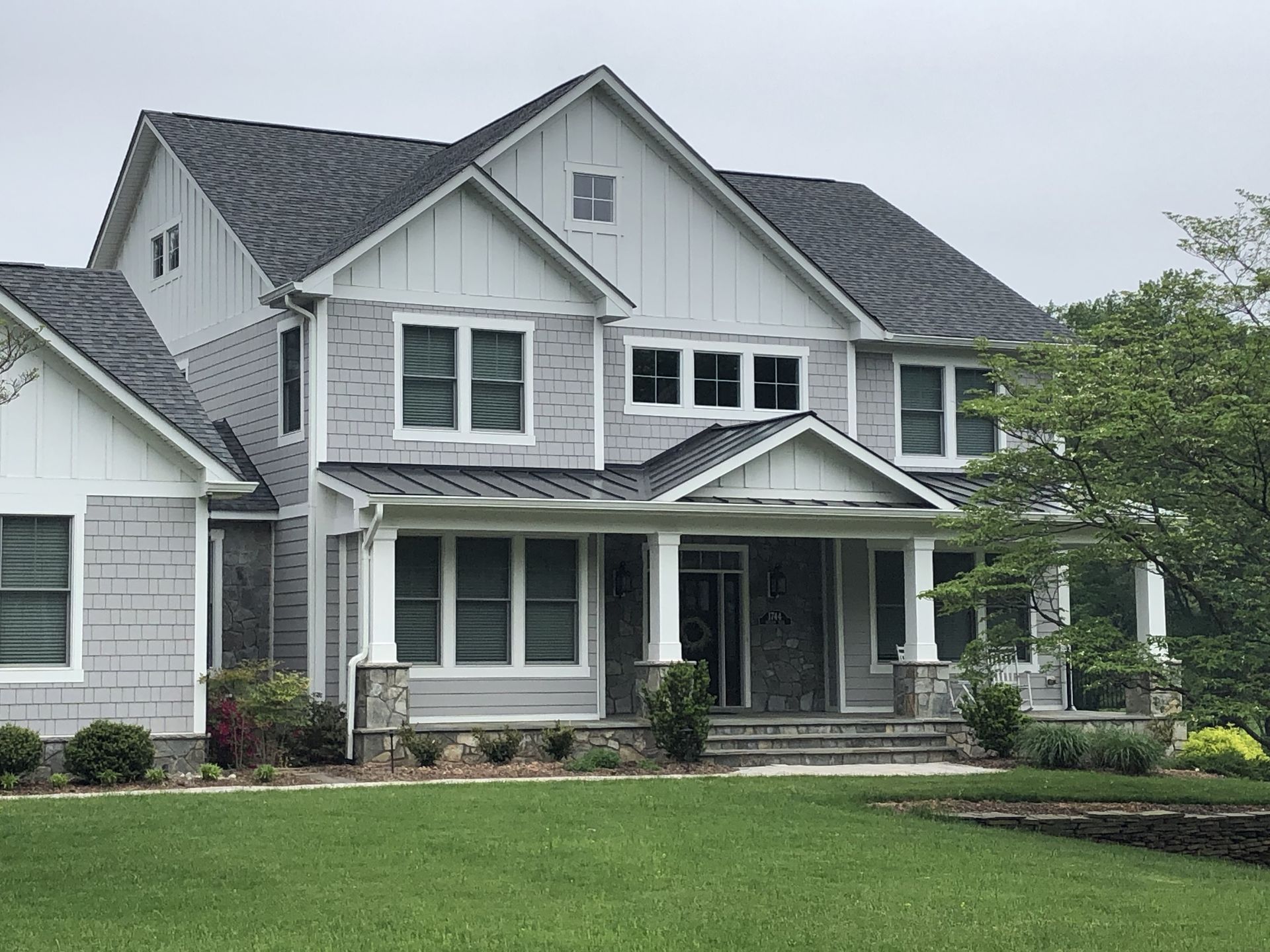 Two-story house with gray siding, white trim, a covered porch, and a well-manicured lawn.
