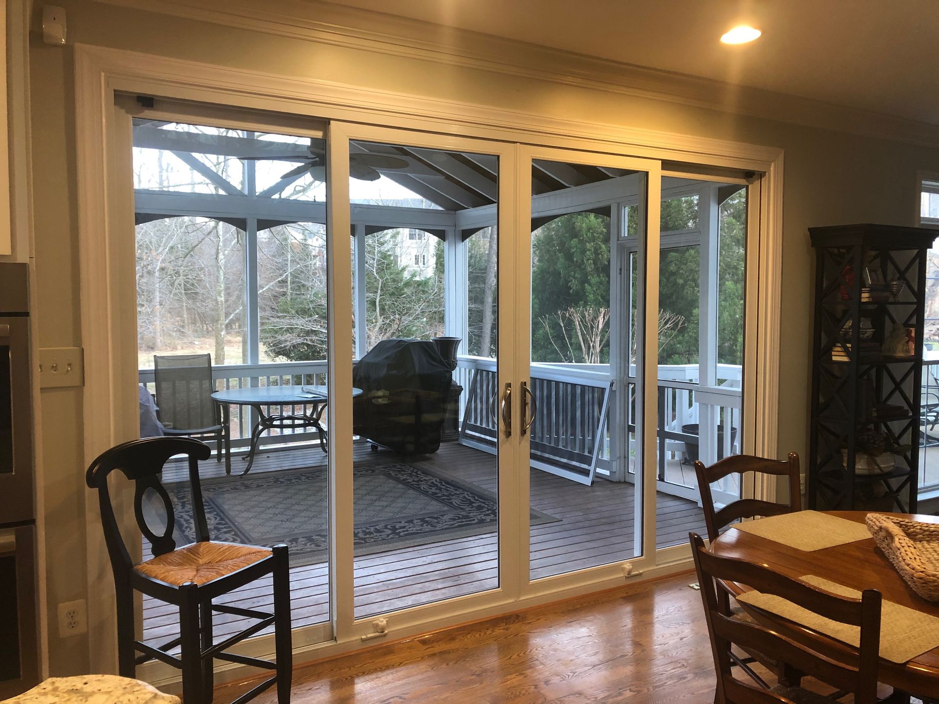 Sliding glass doors open to a screened porch with outdoor furniture; wood floors, beige walls.