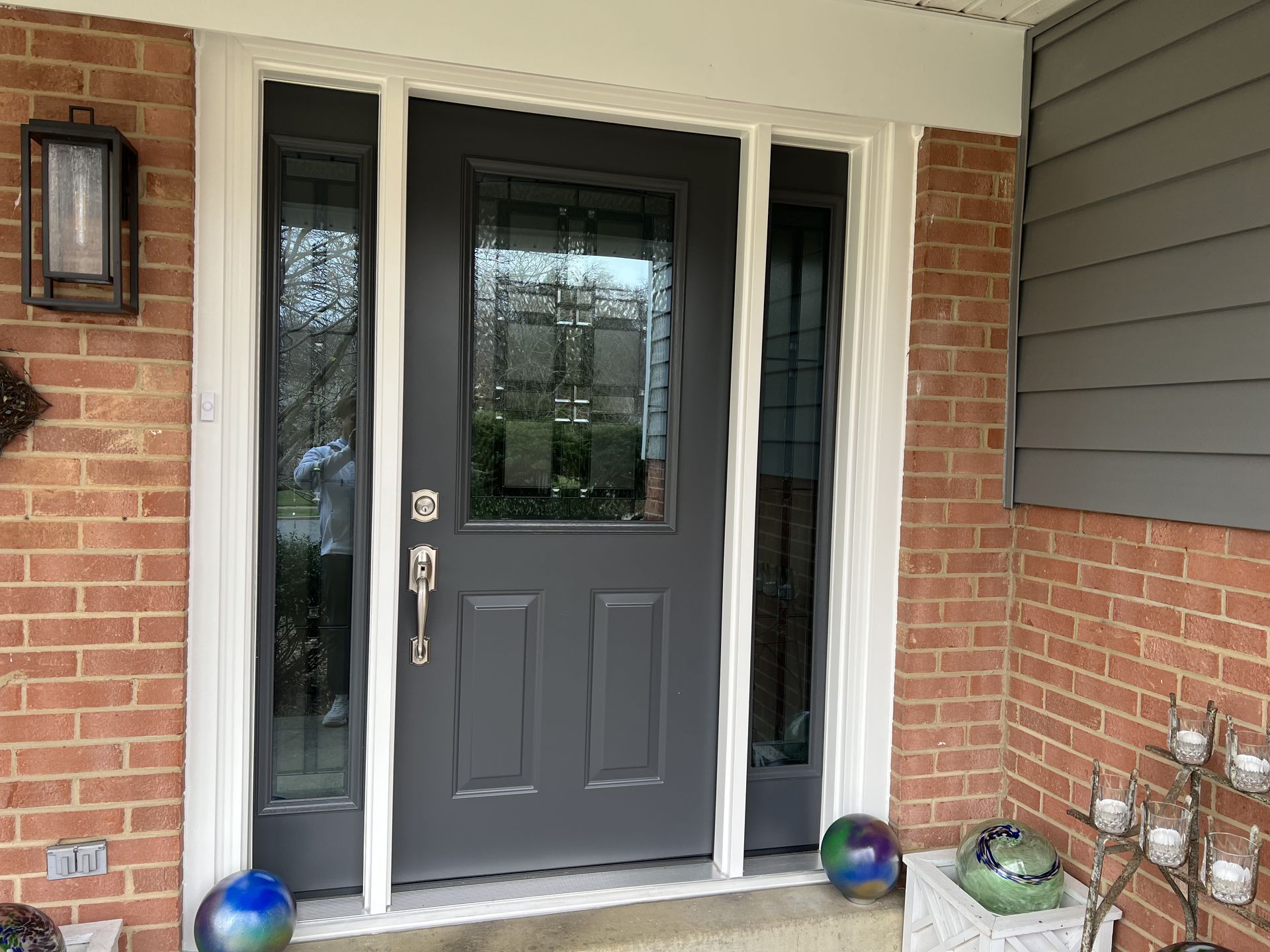 Gray front door with sidelights, brick exterior, and decorative elements.