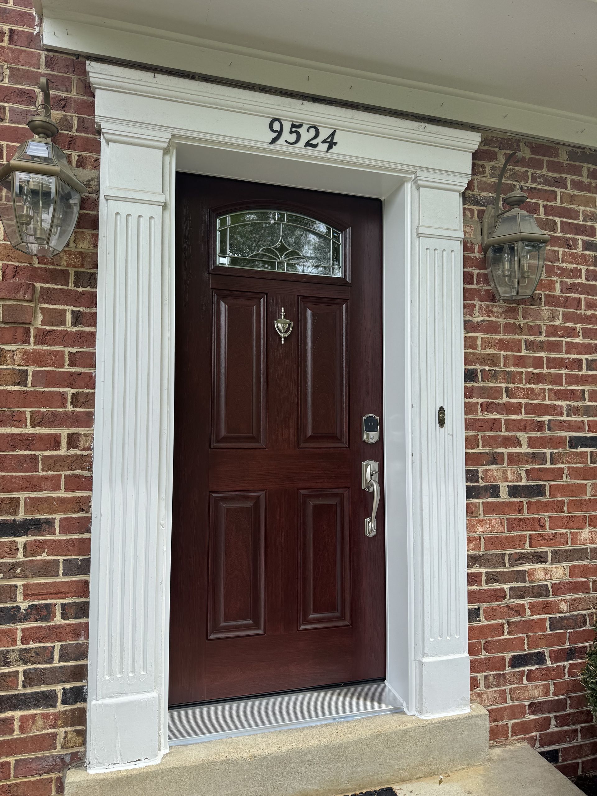 Brown door with glass panel, white trim, brick wall, address numbers 
