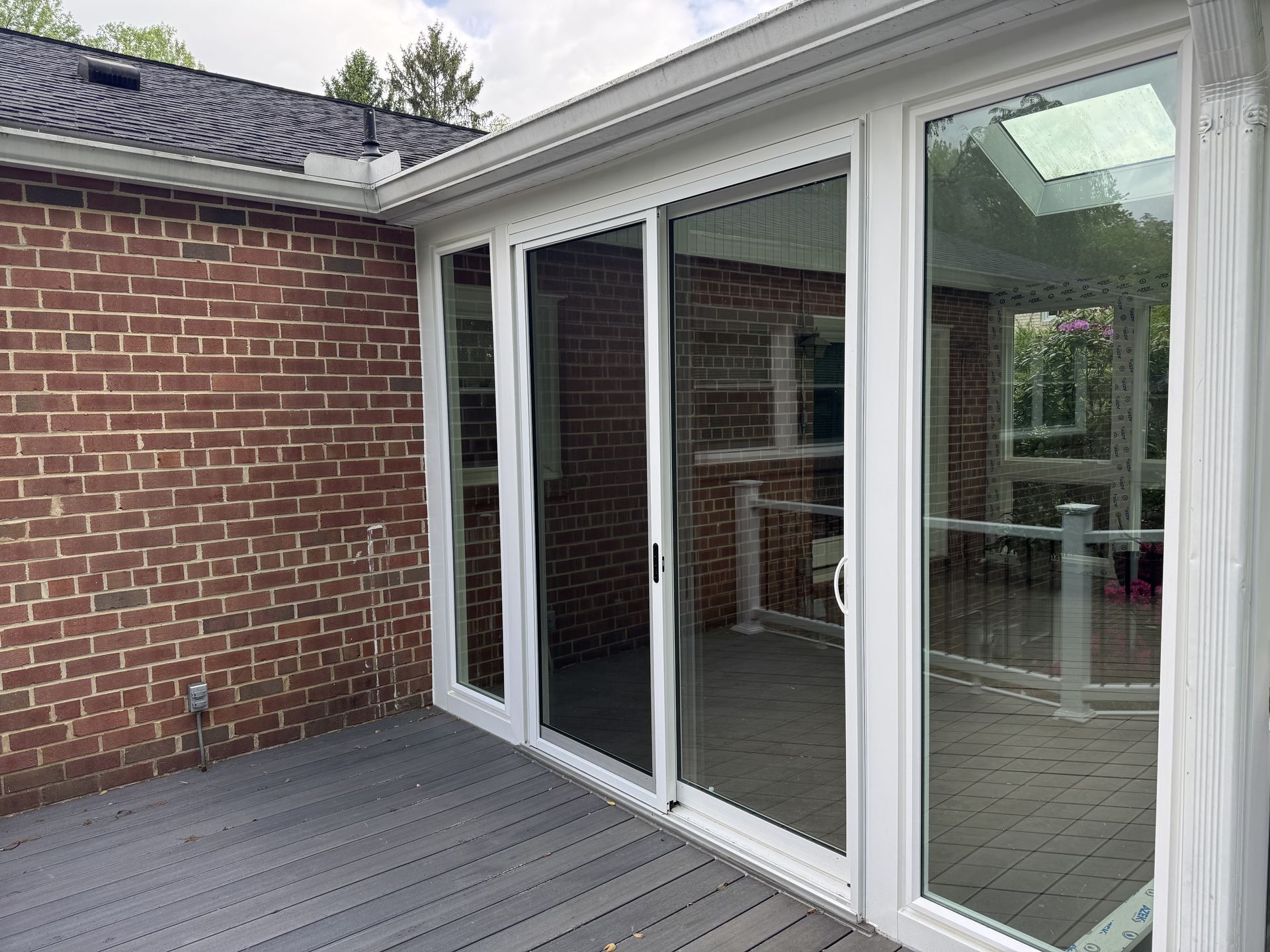 Brick wall, sliding glass doors, and gray deck with white frames.