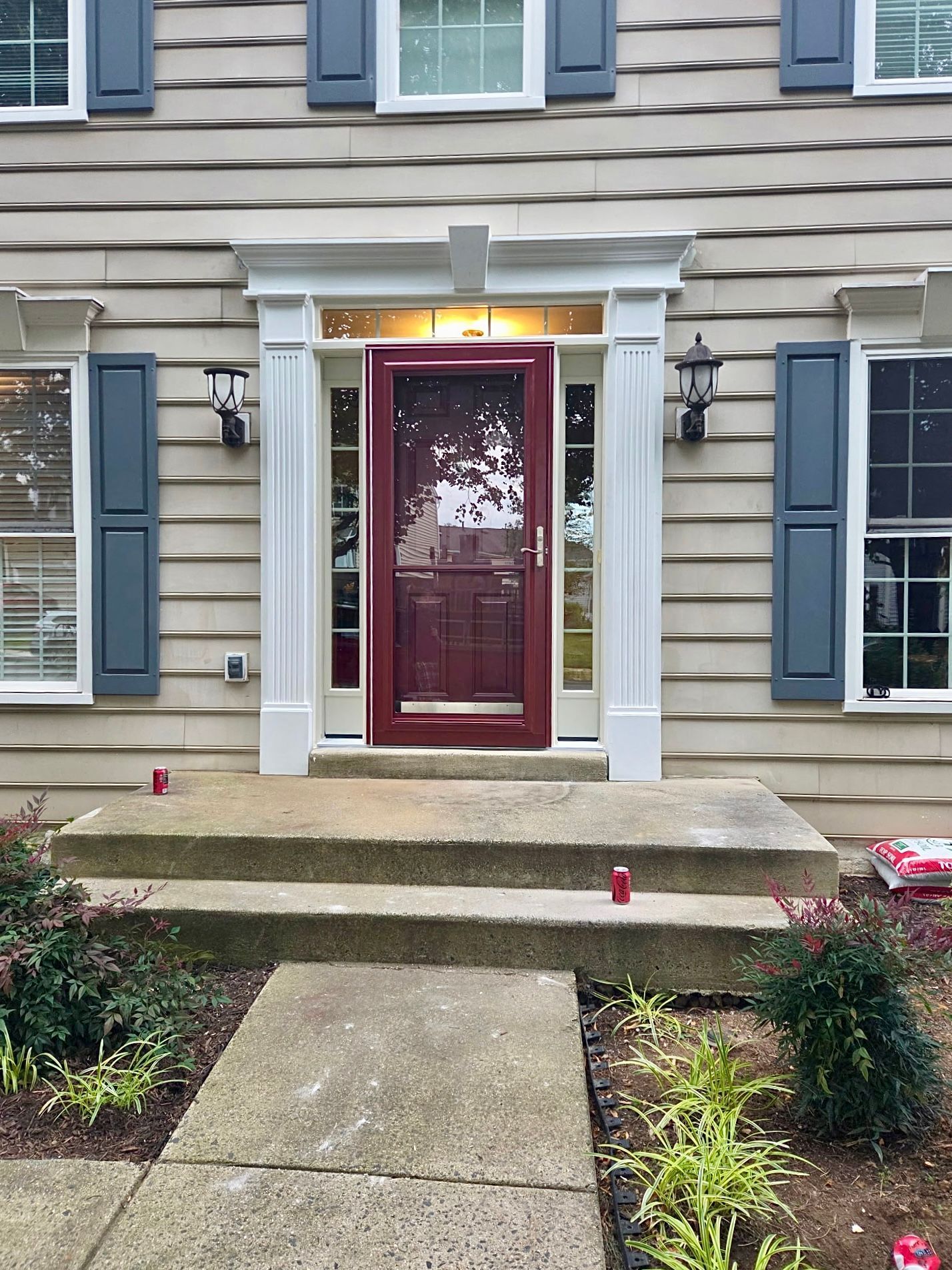 Front entrance of a house with a red door, white trim, gray siding, and concrete steps and walkway.