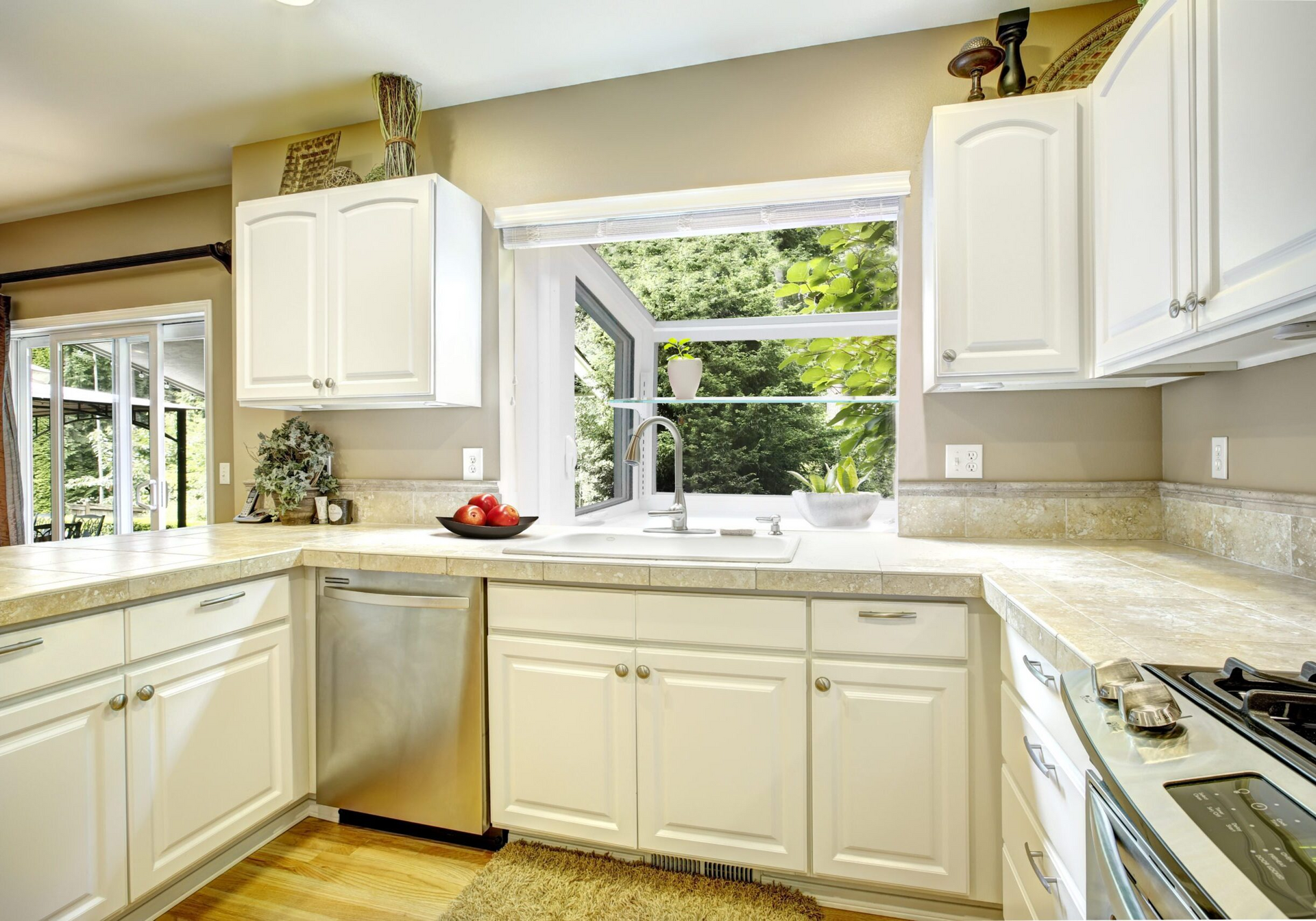 A kitchen with white cabinets , stainless steel appliances , granite counter tops and a large window.