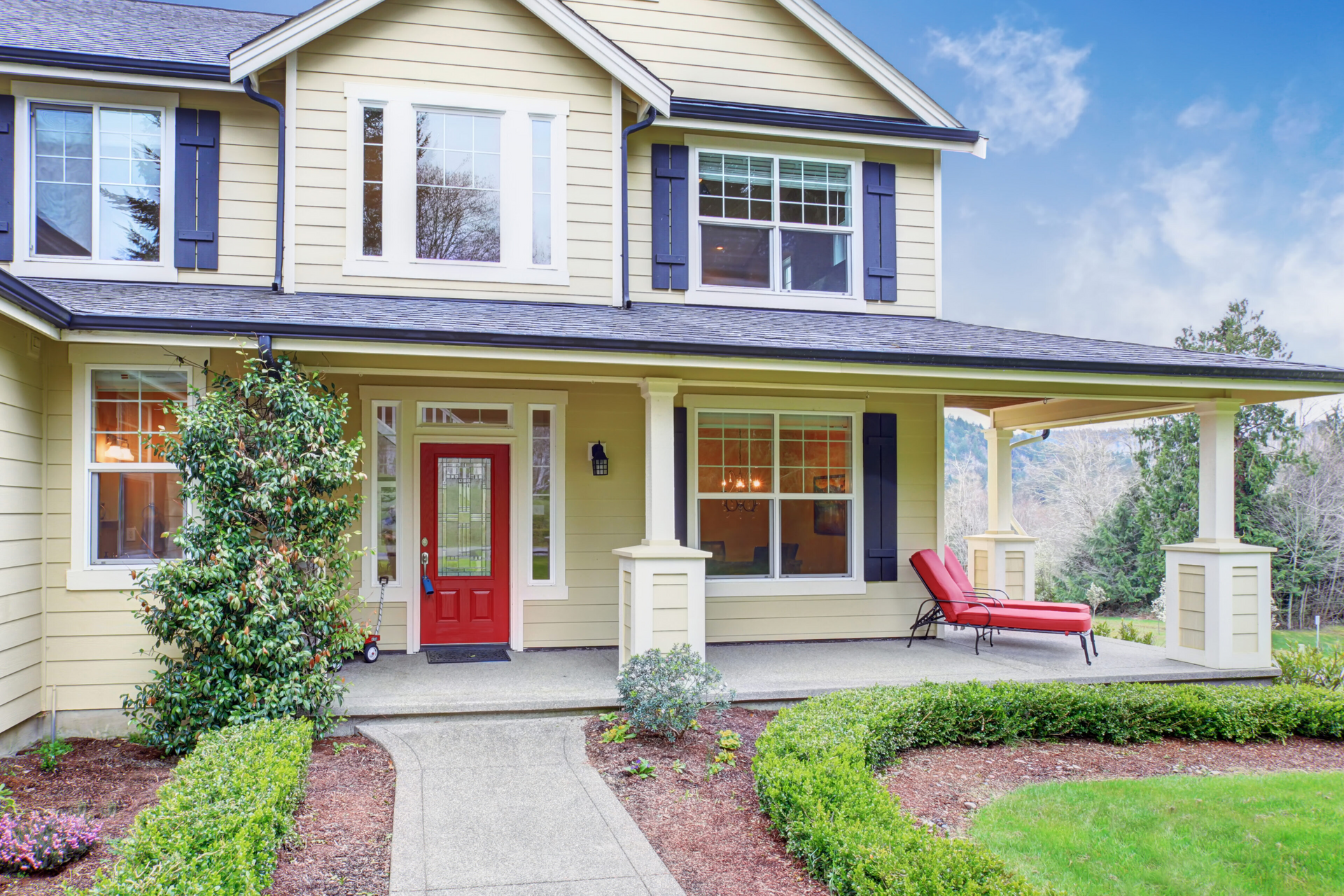 A large yellow house with a red door and a large porch.