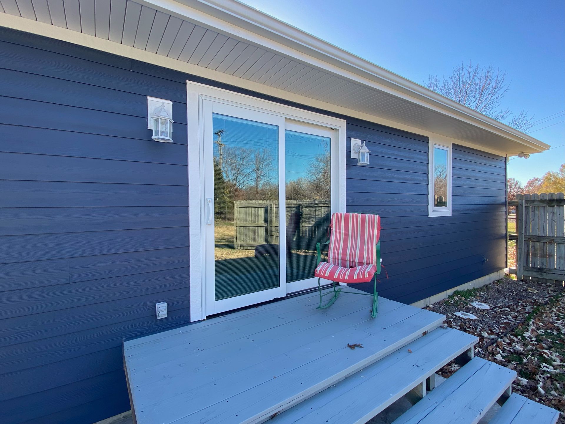 a blue house with a sliding glass door and a chair on the porch