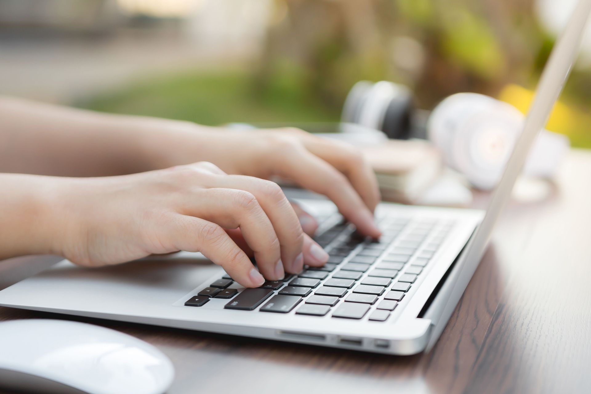 A person is typing on a laptop computer on a wooden table.