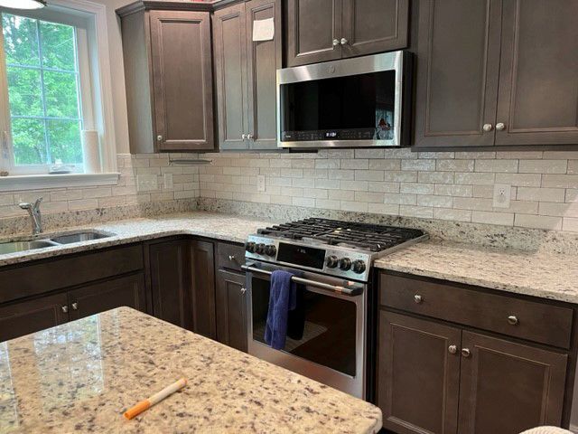 A kitchen with granite counter tops, stainless steel appliances, and gray cabinets.