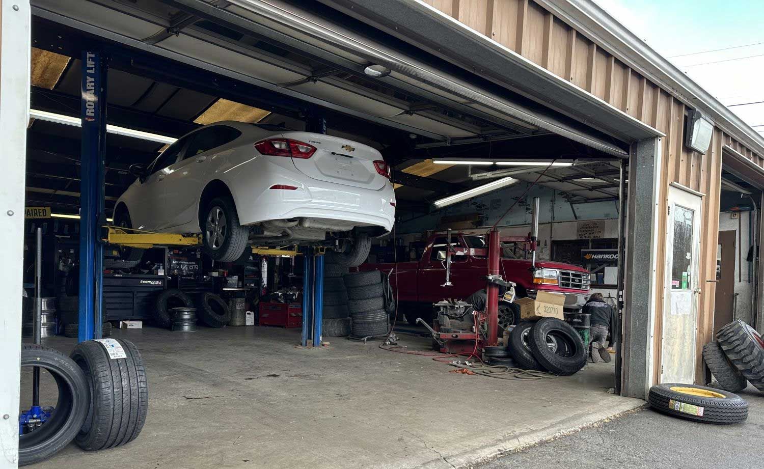 White car on a lift inside a garage. Tires and equipment are visible.