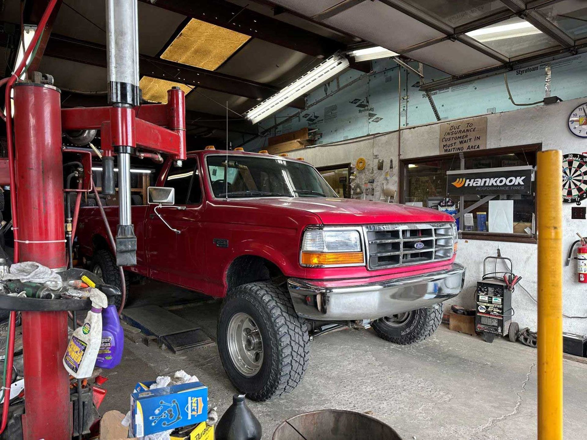 Red pickup truck inside a garage bay, on a lift. Tools and equipment visible.