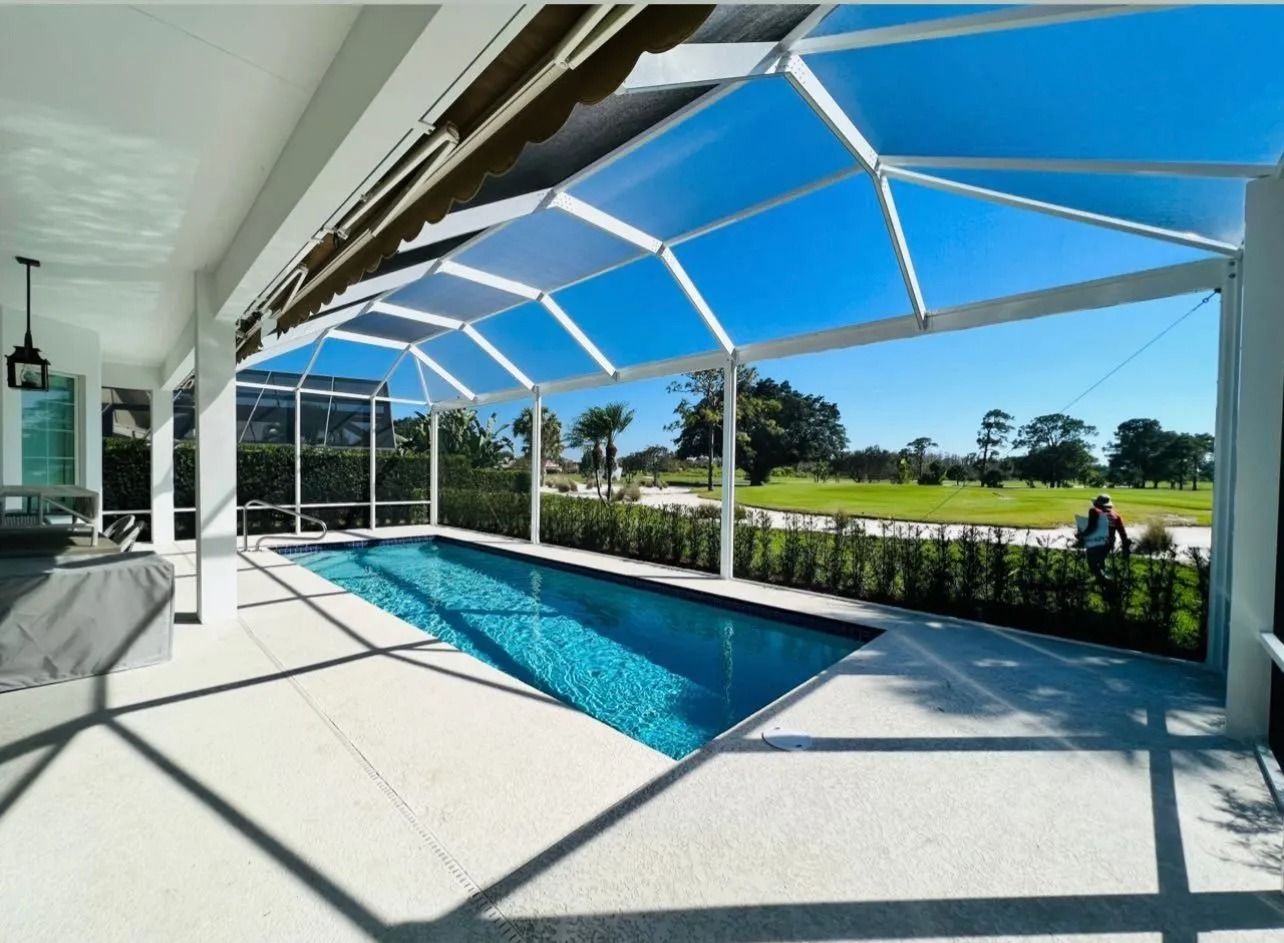 Pool under a screened enclosure with a golf course view. Blue water, white framing, bright sunny day.