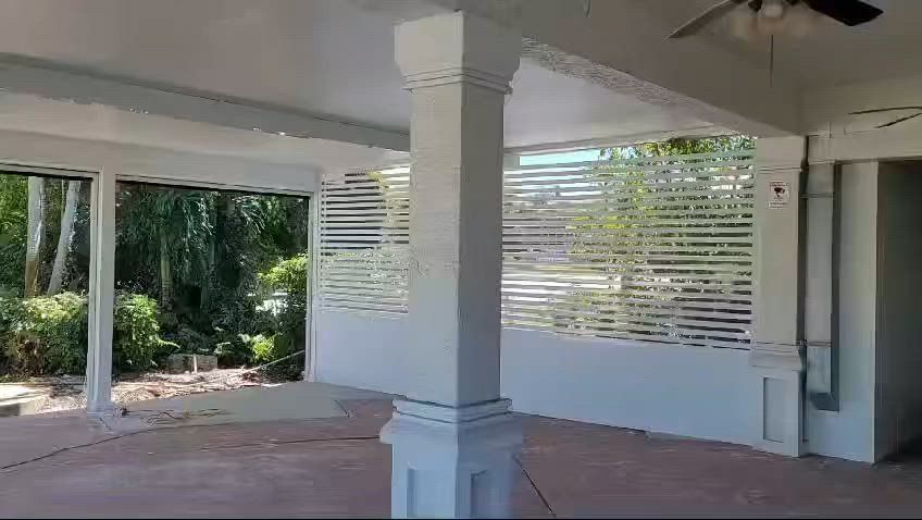 White porch with slatted walls, columns, and a view of greenery.