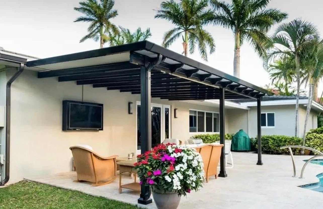 Patio with black pergola, outdoor seating, TV on wall, and palm trees.