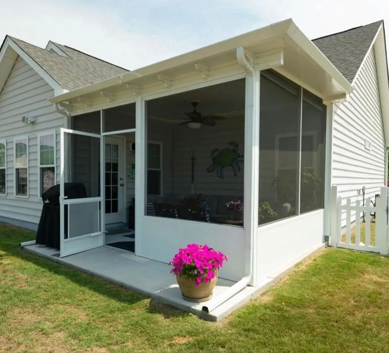 Screened porch addition on a white house, with a potted pink flower and open screen door.