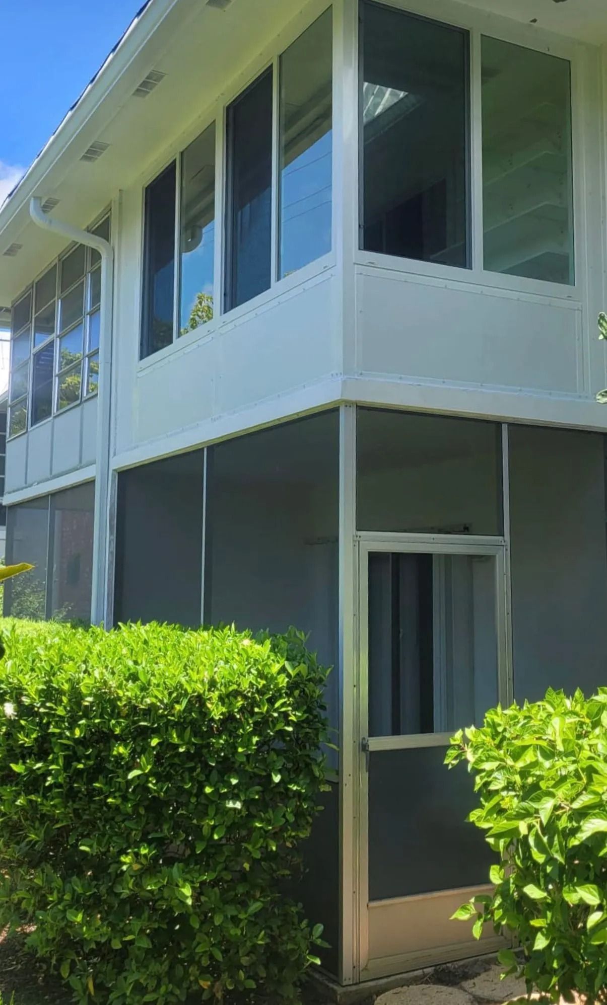 White house with screened porch, large windows, and green bushes in front.