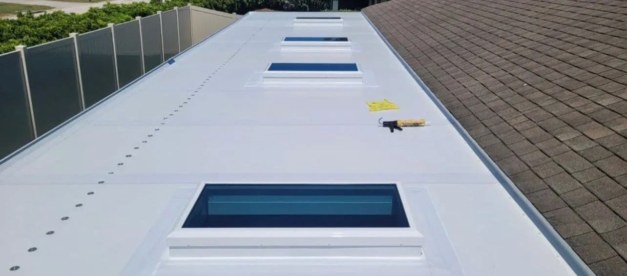 White roof with four skylights, next to a brown shingled roof.