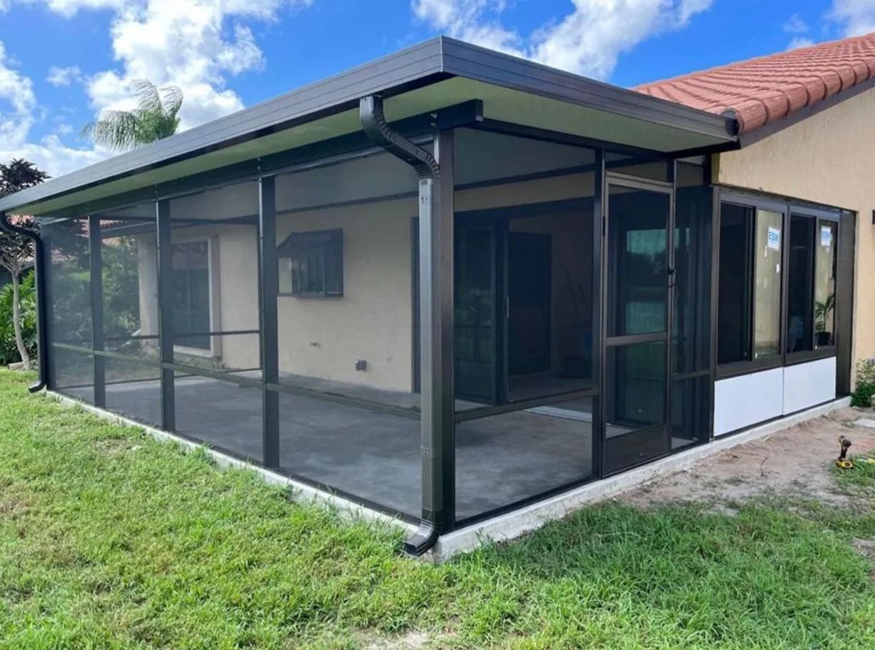 Screened-in patio with dark framing and screens, attached to a house with a tile roof and surrounded by grass.
